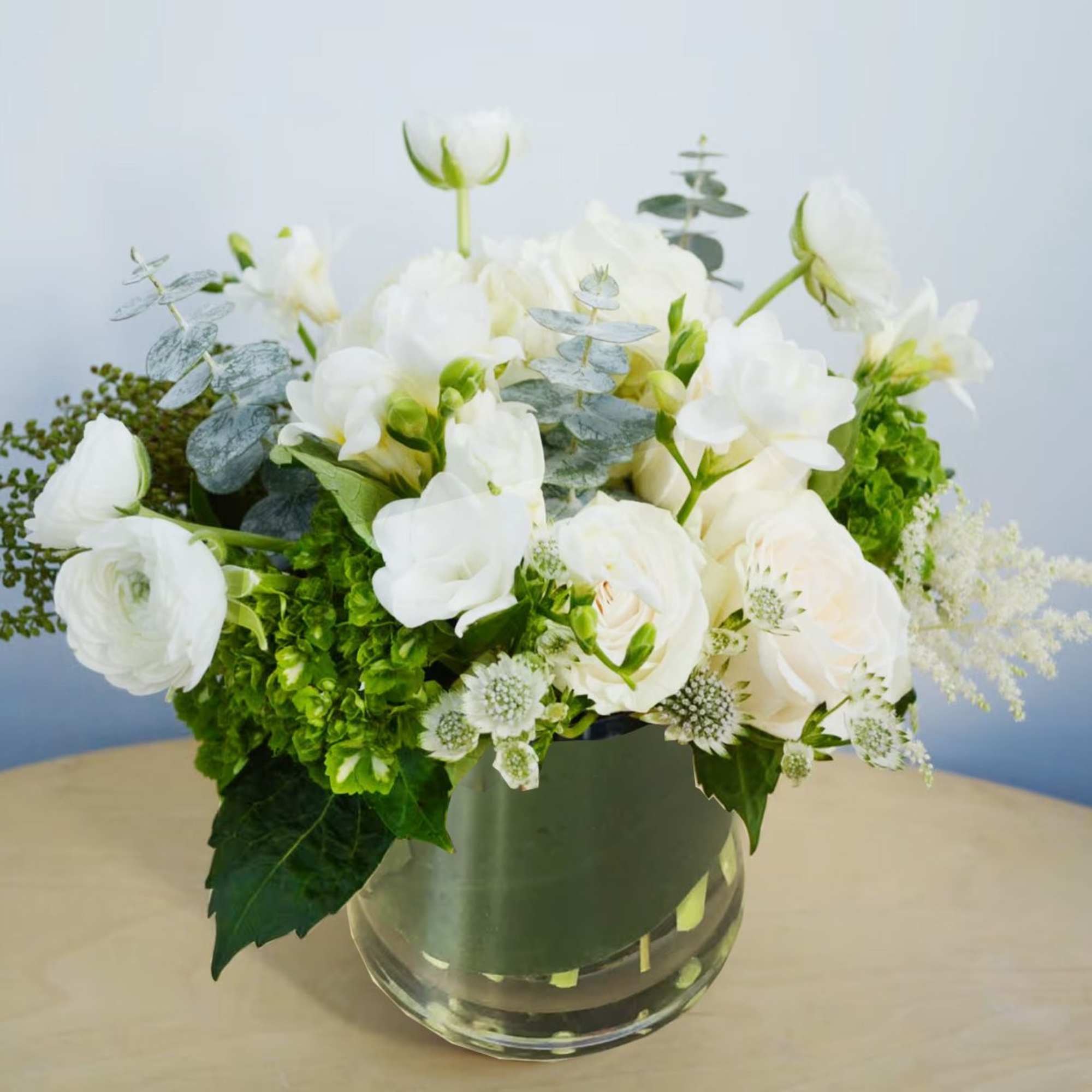 White flowers arranged in a clear glass vase with green accents, photo 2 of 2