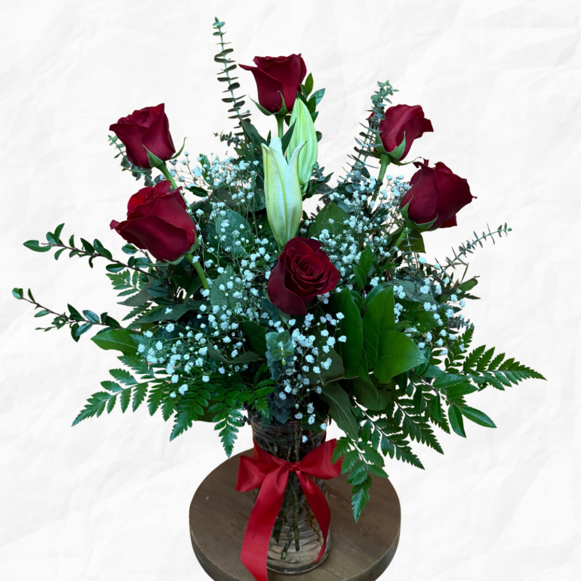 Bouquet of red roses and white lilies in a glass vase with a red ribbon