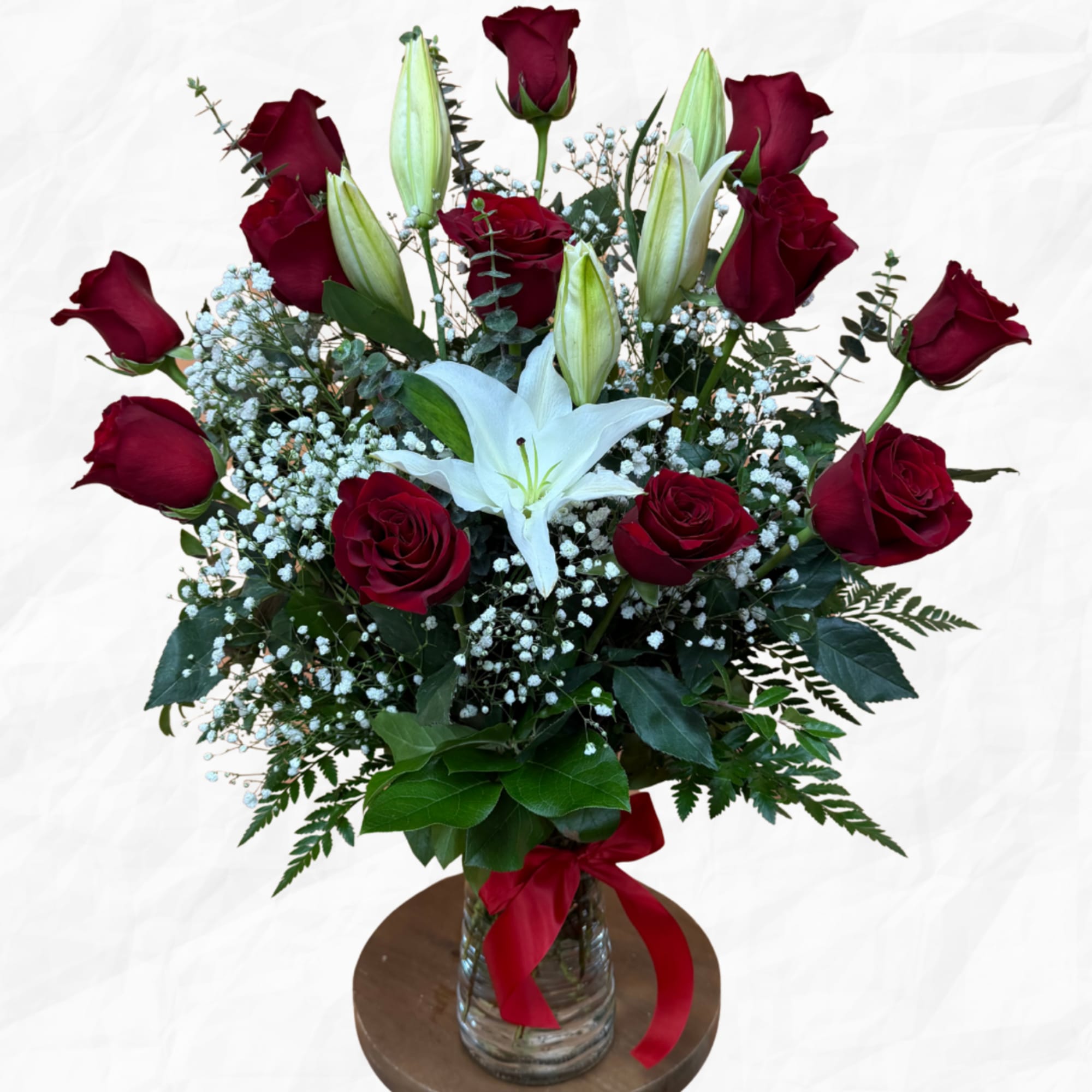Red roses and white lilies in a glass vase with a red ribbon