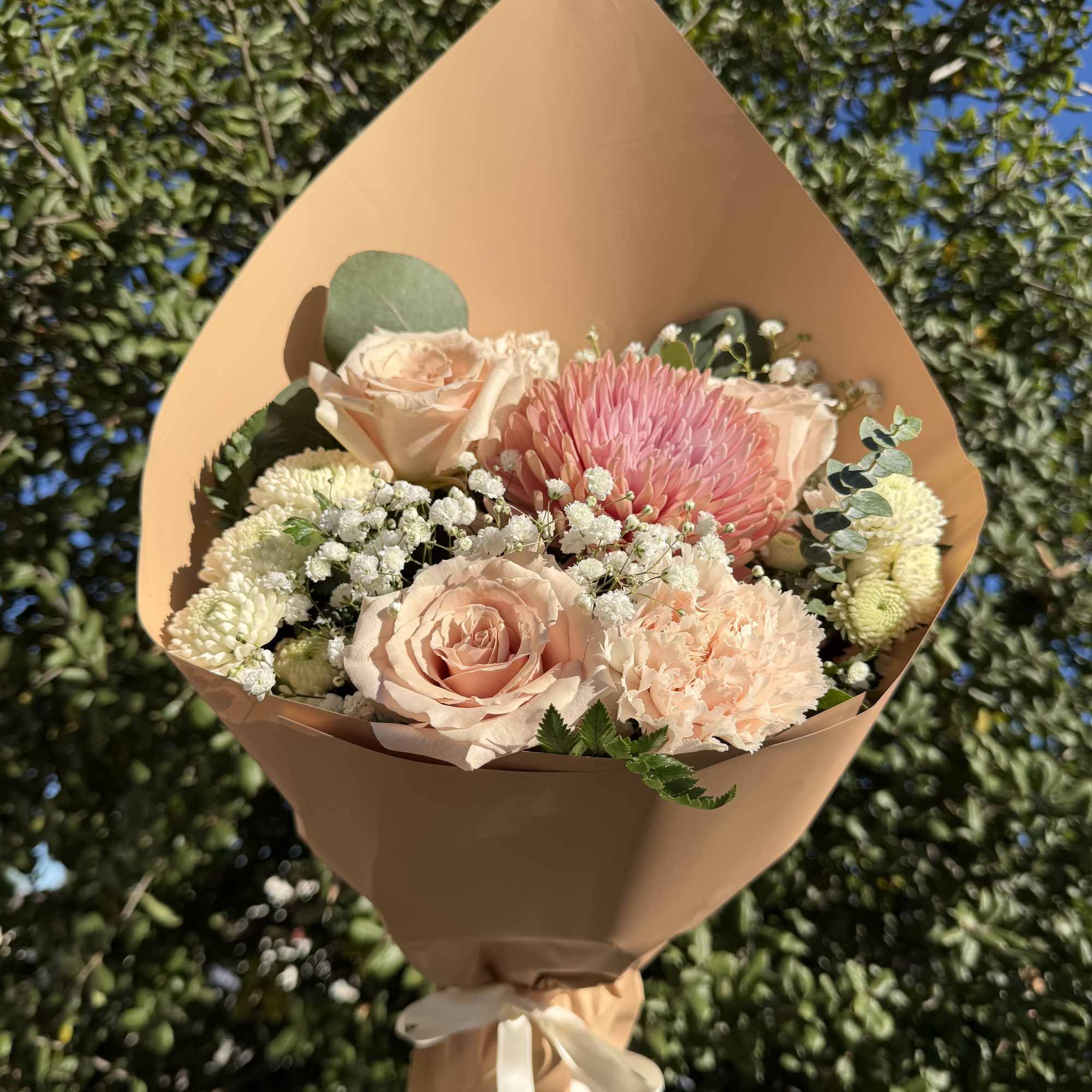 Peach and pink bouquet with roses and chrysanthemums wrapped in tan paper