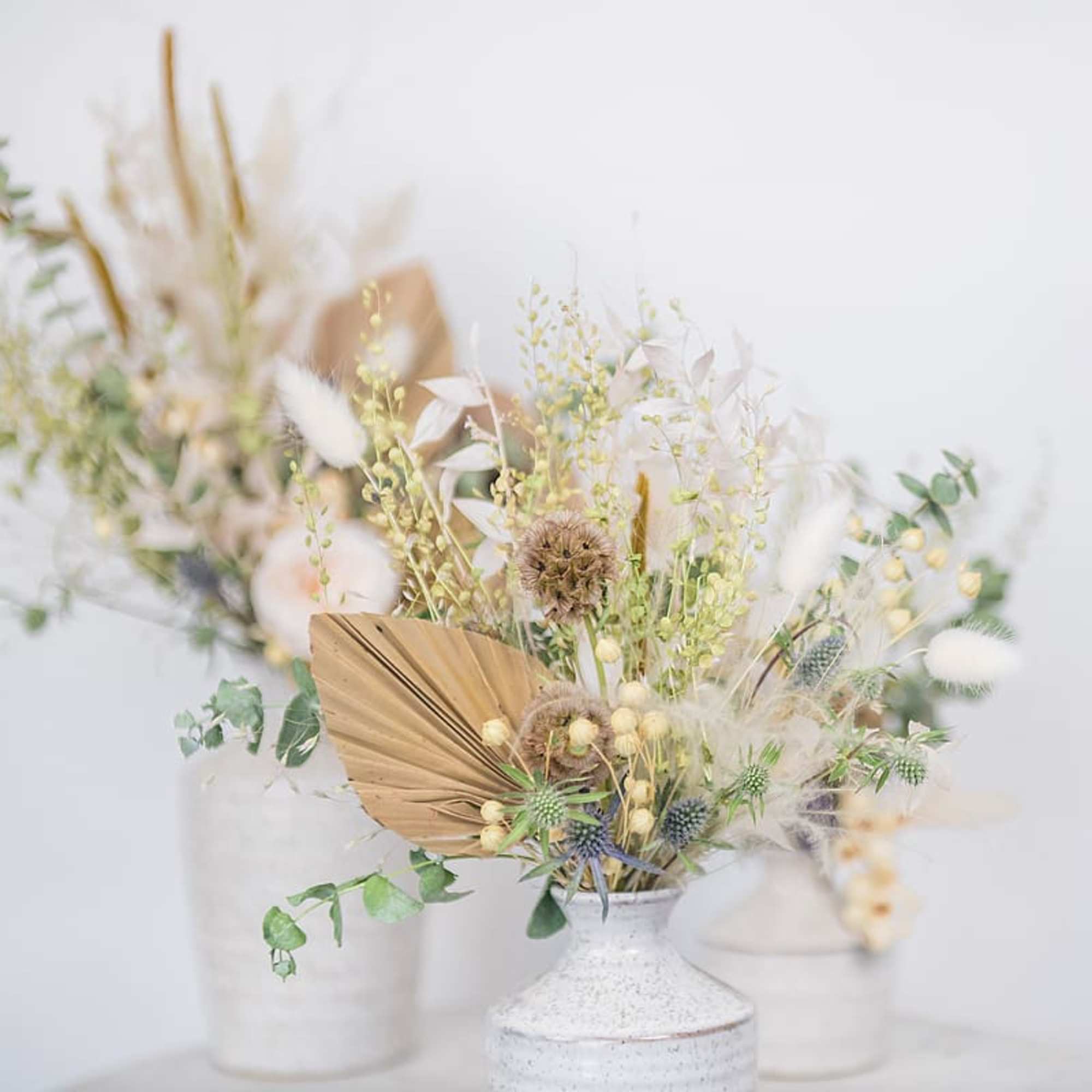 Dried floral arrangement in a white vase with beige and white accents