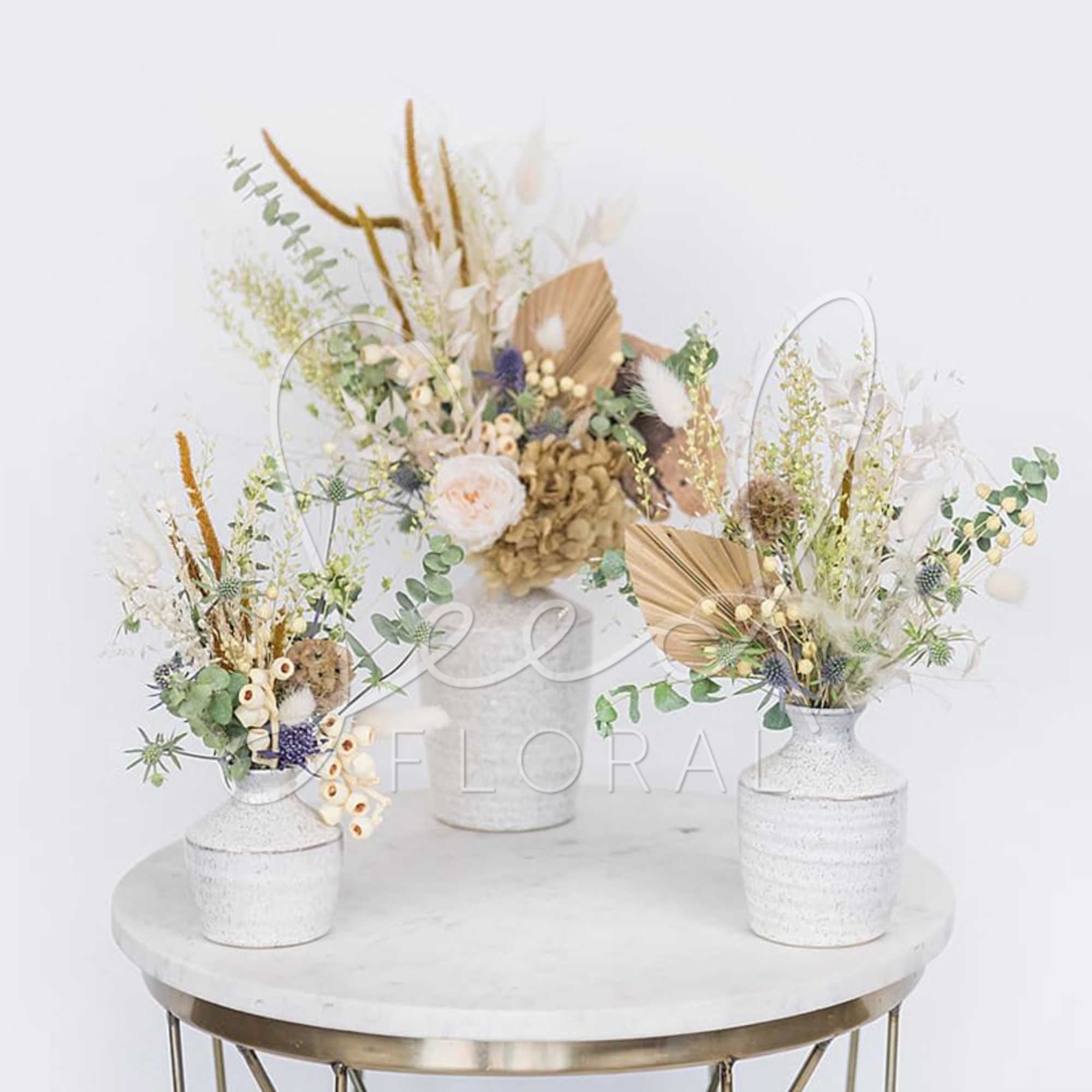 Three dried floral arrangements in white vases on a round table