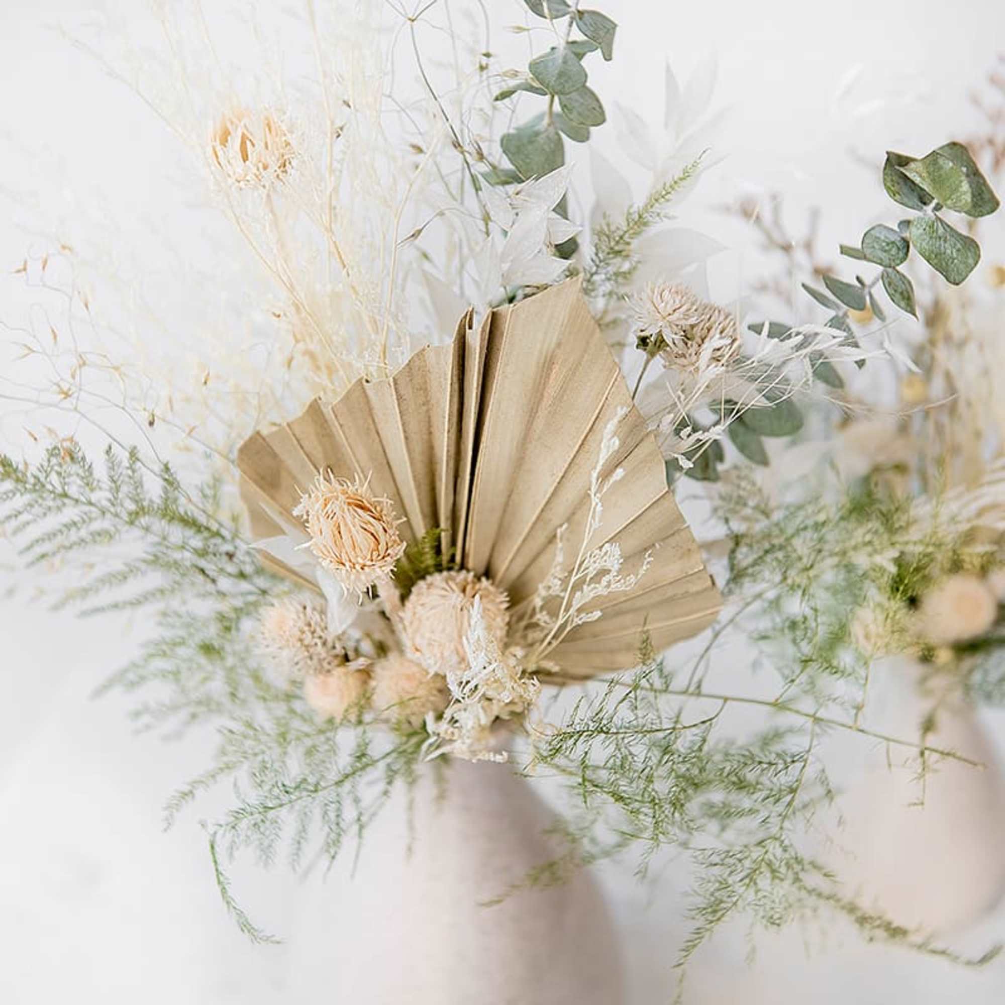Dried floral arrangement with beige fan-shaped paper and pale blooms