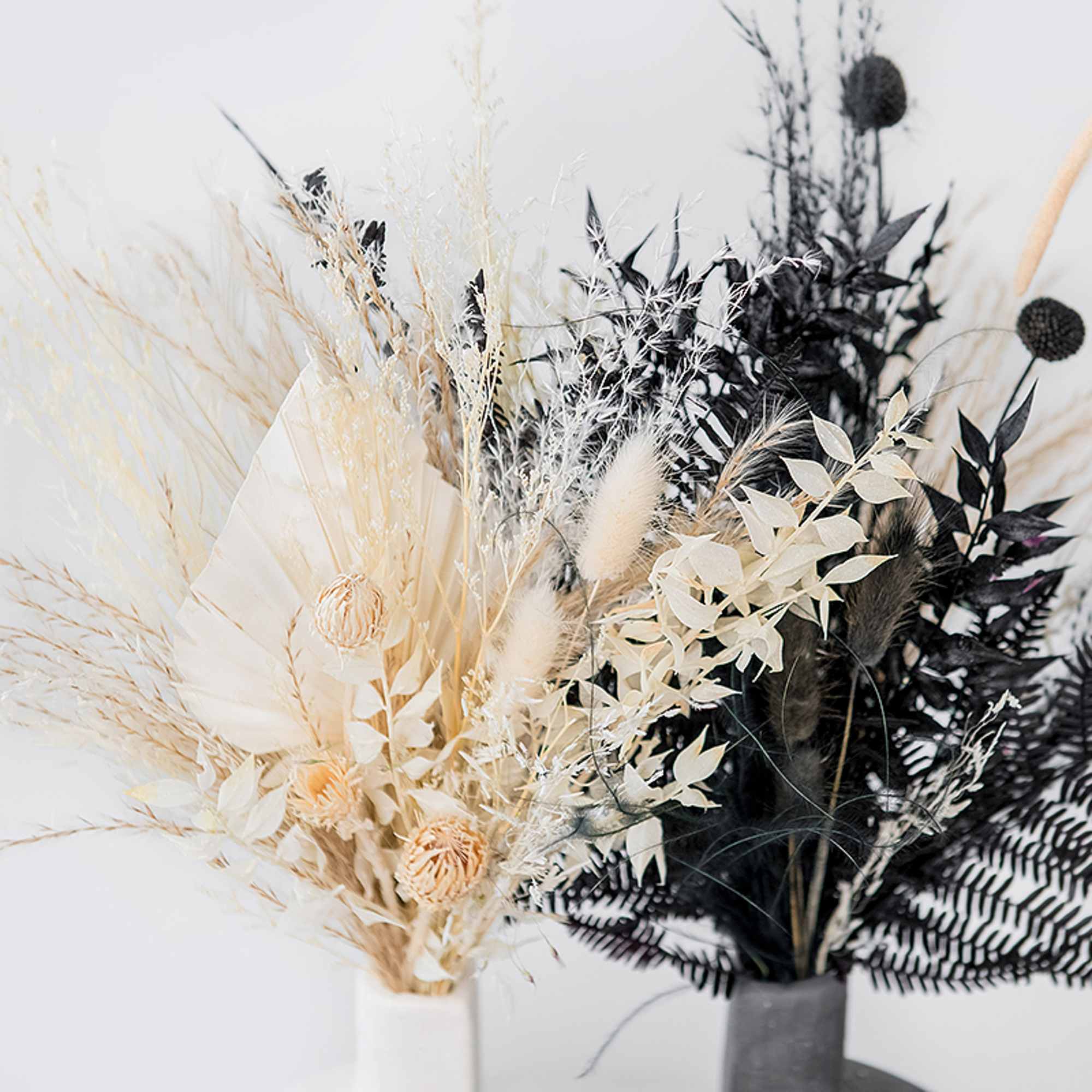 Two dried floral arrangements in white and black tones in vases