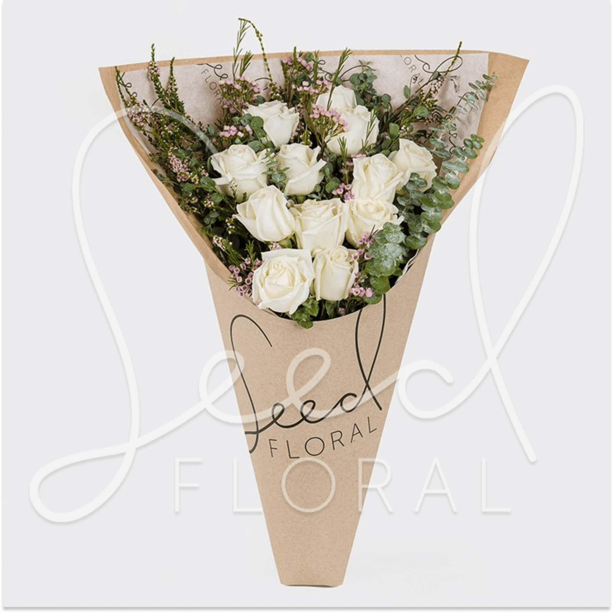 Wrapped bouquet of white roses with small pink accents in a kraft paper sleeve