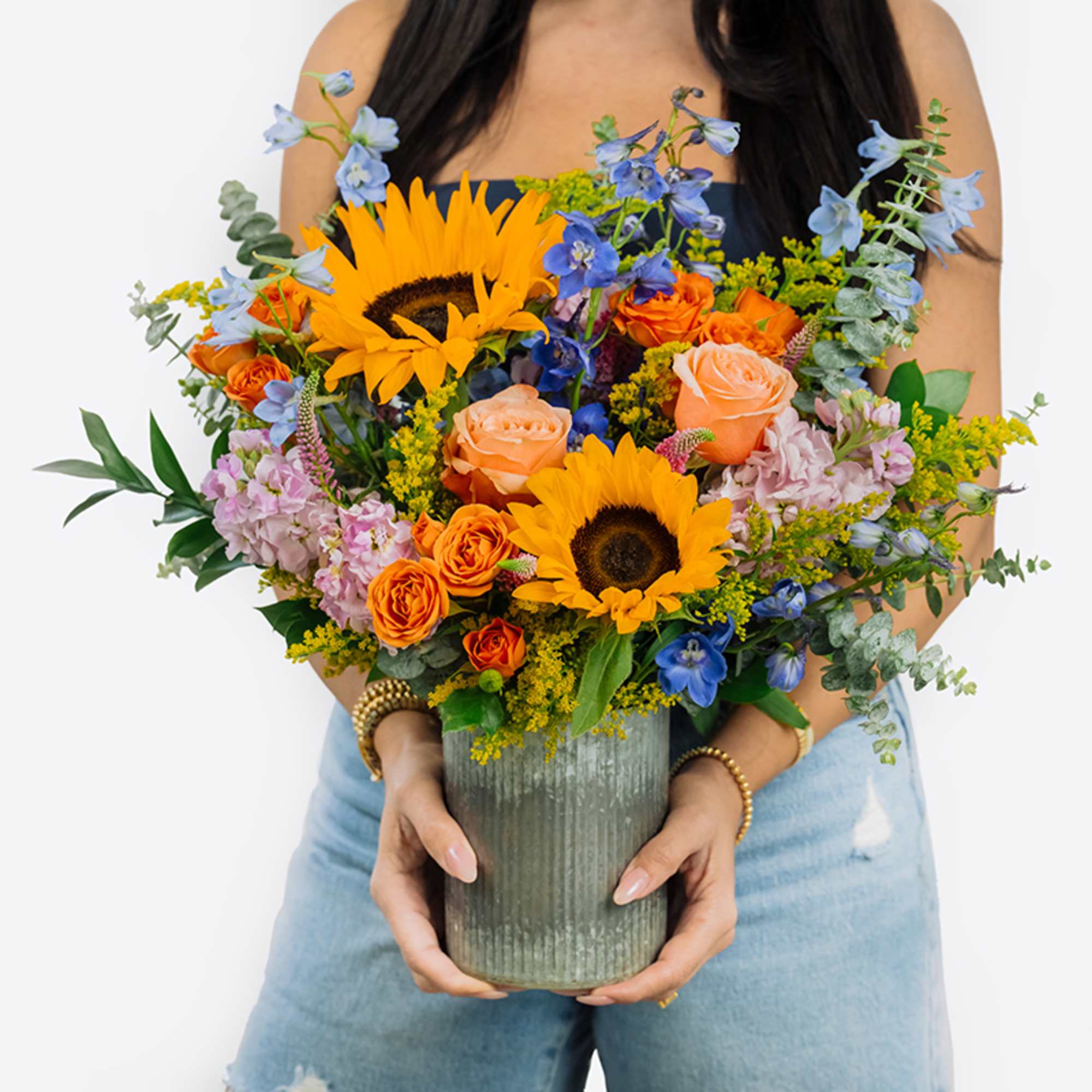Bouquet with sunflowers, orange roses, and blue flowers in a ribbed vase