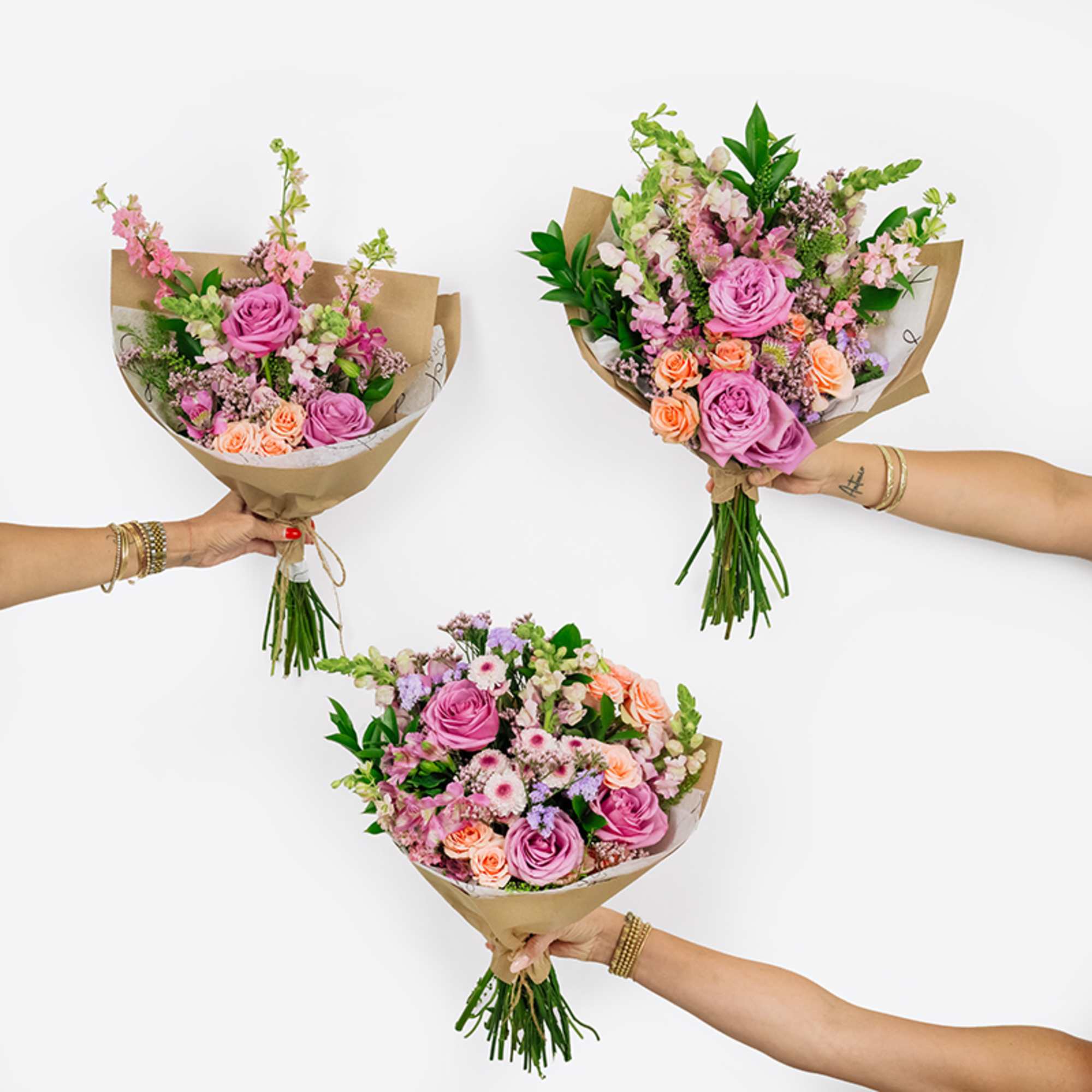 Three hand-tied bouquets of pink and peach flowers wrapped in brown paper