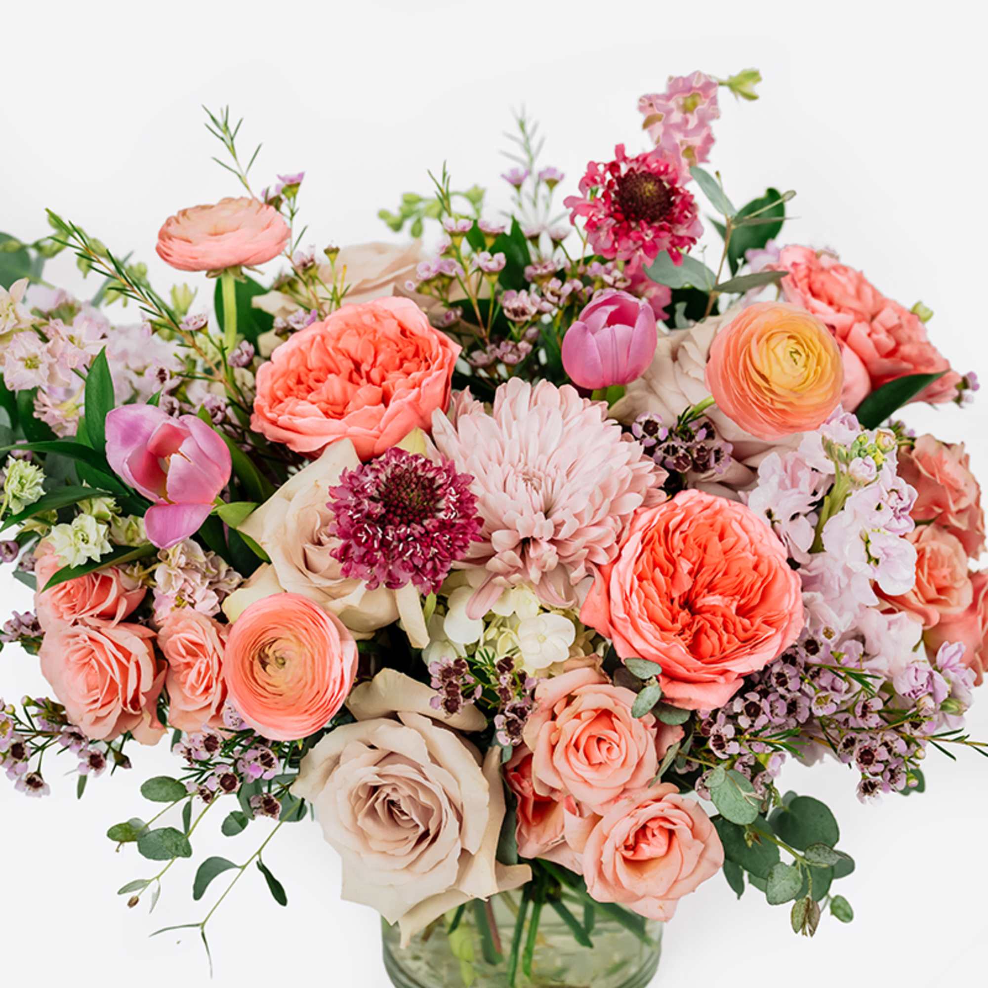 Mixed bouquet of coral, pink, and cream flowers in a glass vase