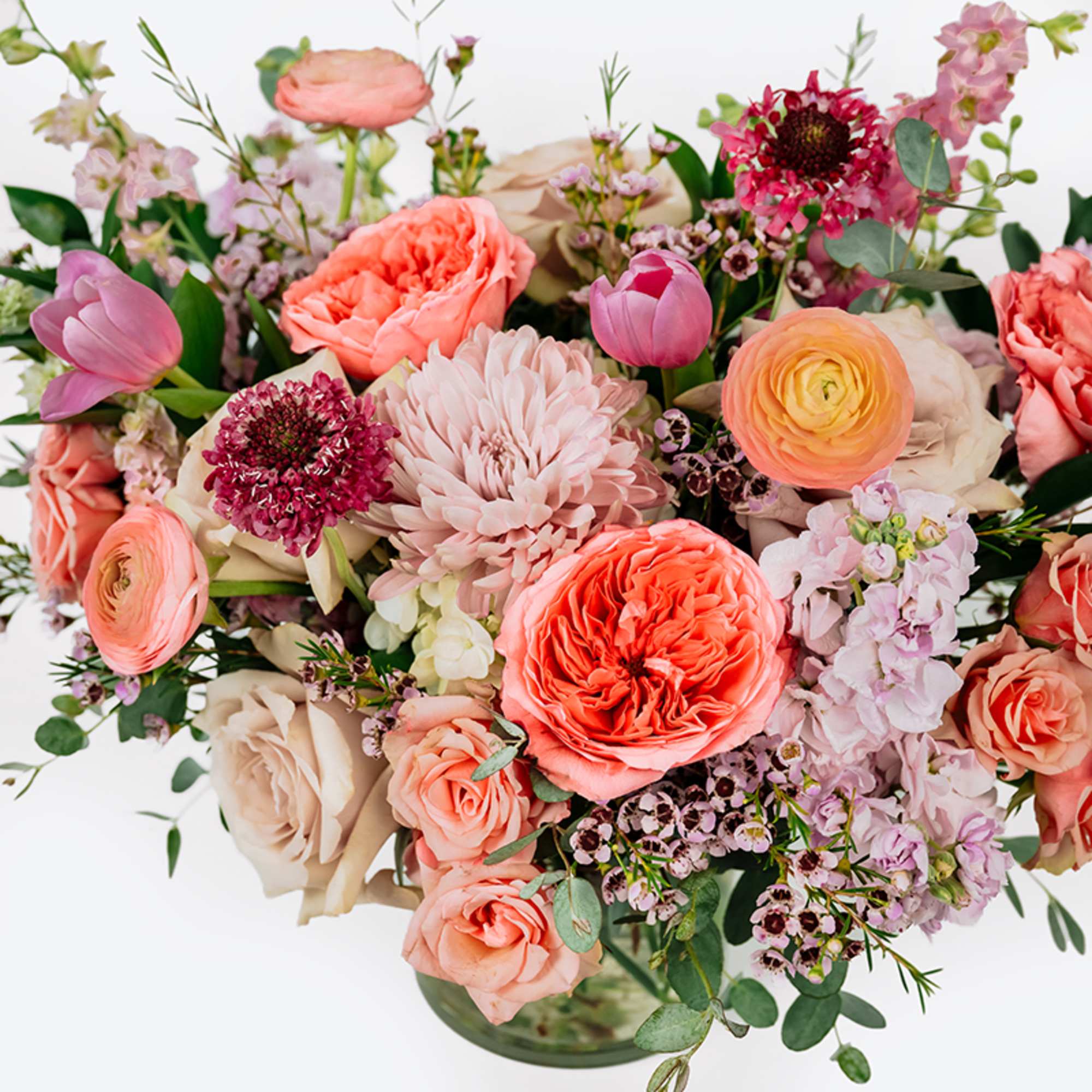 Mixed bouquet of pink, peach, and cream flowers in a glass vase