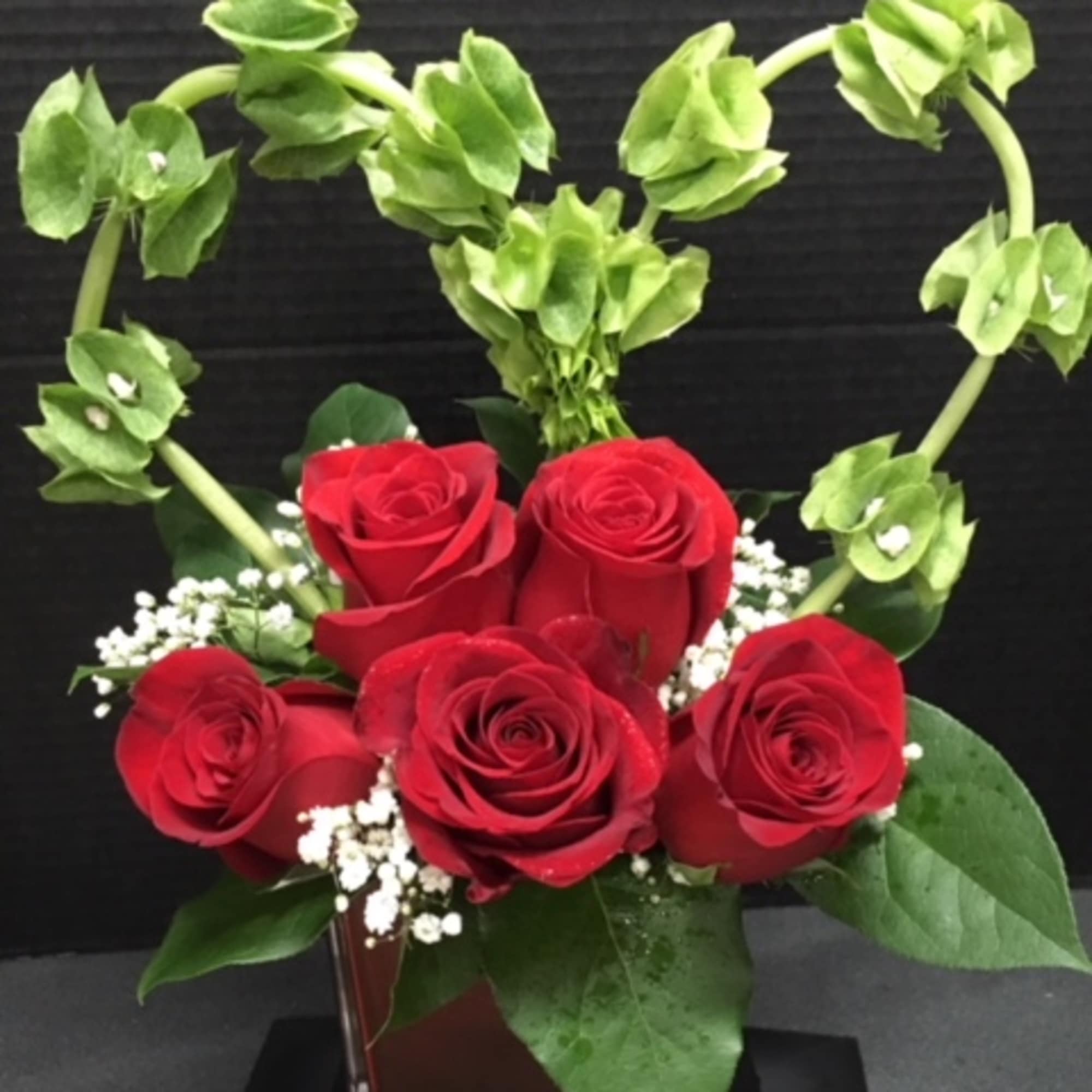 Red roses in a vase with a heart-shaped green floral accent