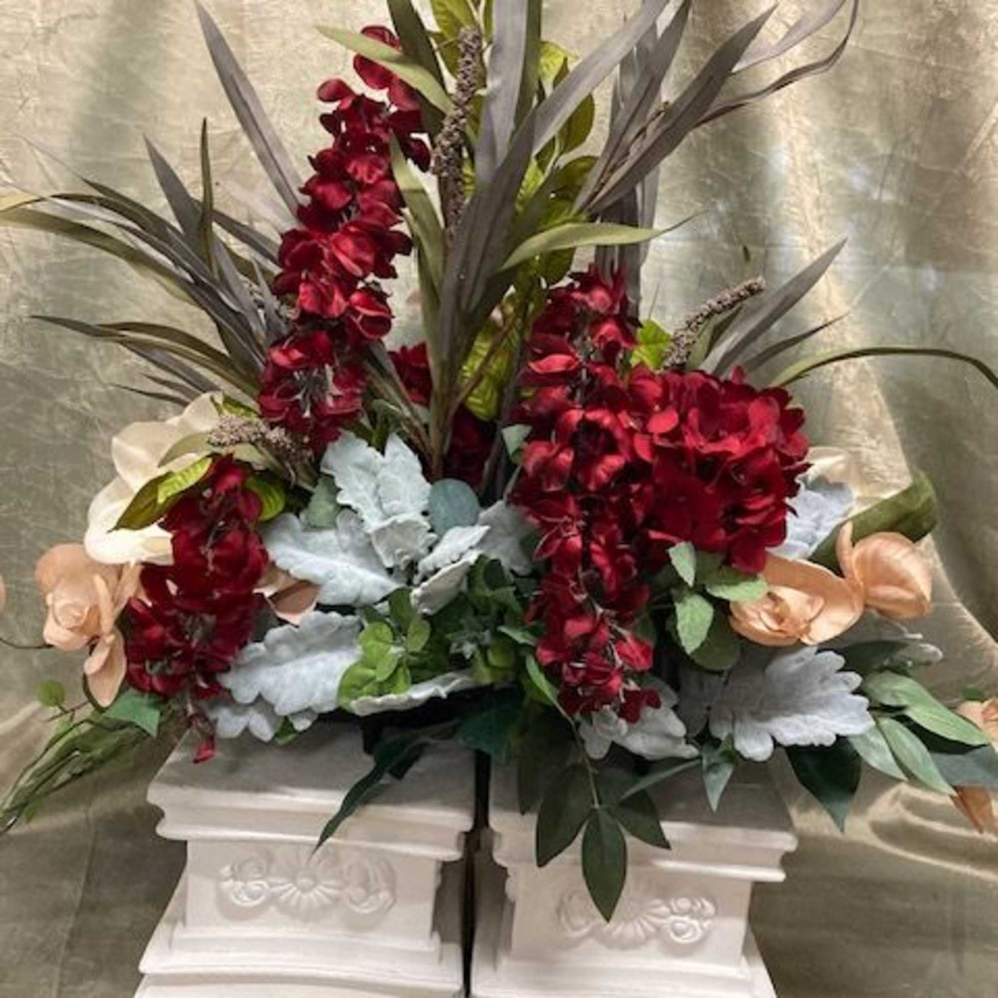 Tall floral arrangement with red orchids and pale flowers in a white pedestal container