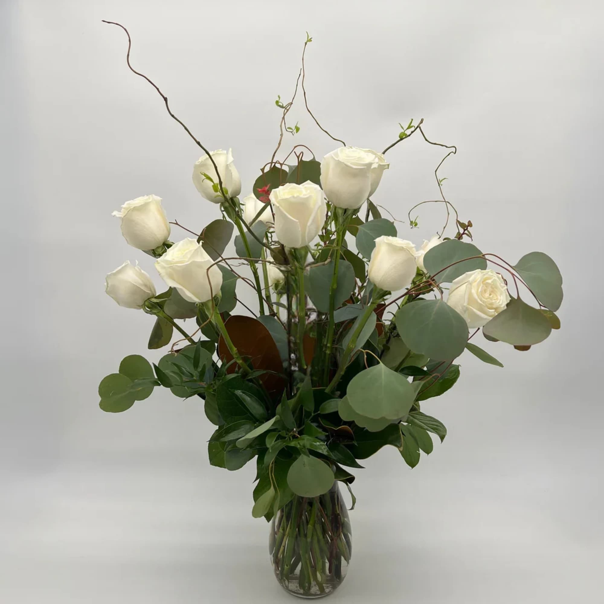 Tall arrangement of white roses with curving branches in a clear glass vase.