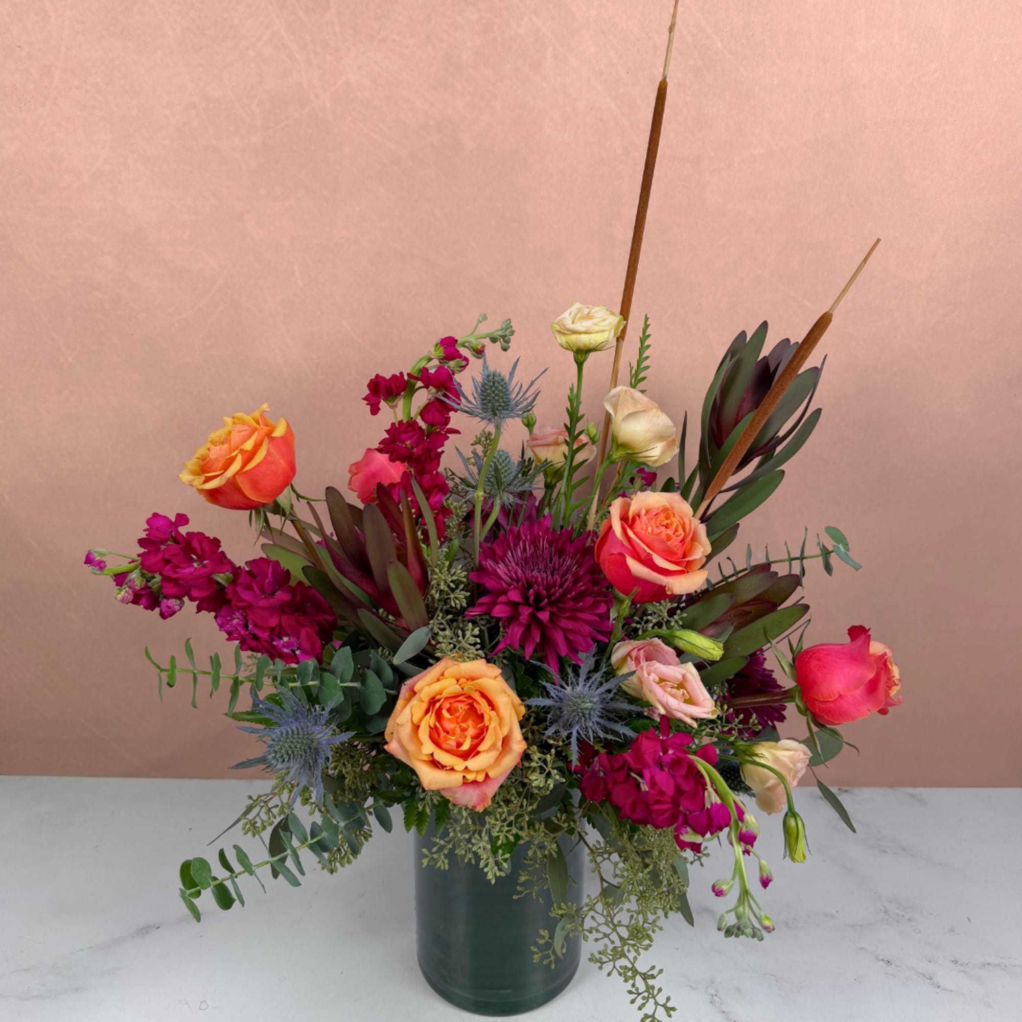 Mixed bouquet of orange and pink roses in a dark green vase
