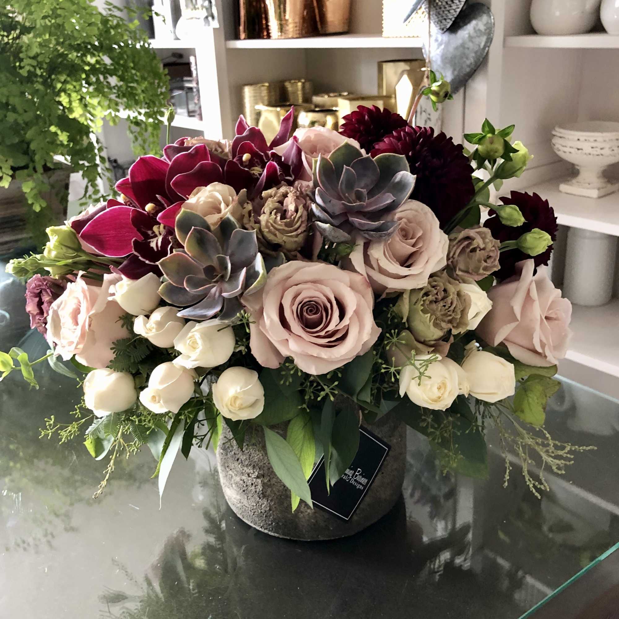 Mixed bouquet with pale roses, dark orchids, and succulents in a stone vase