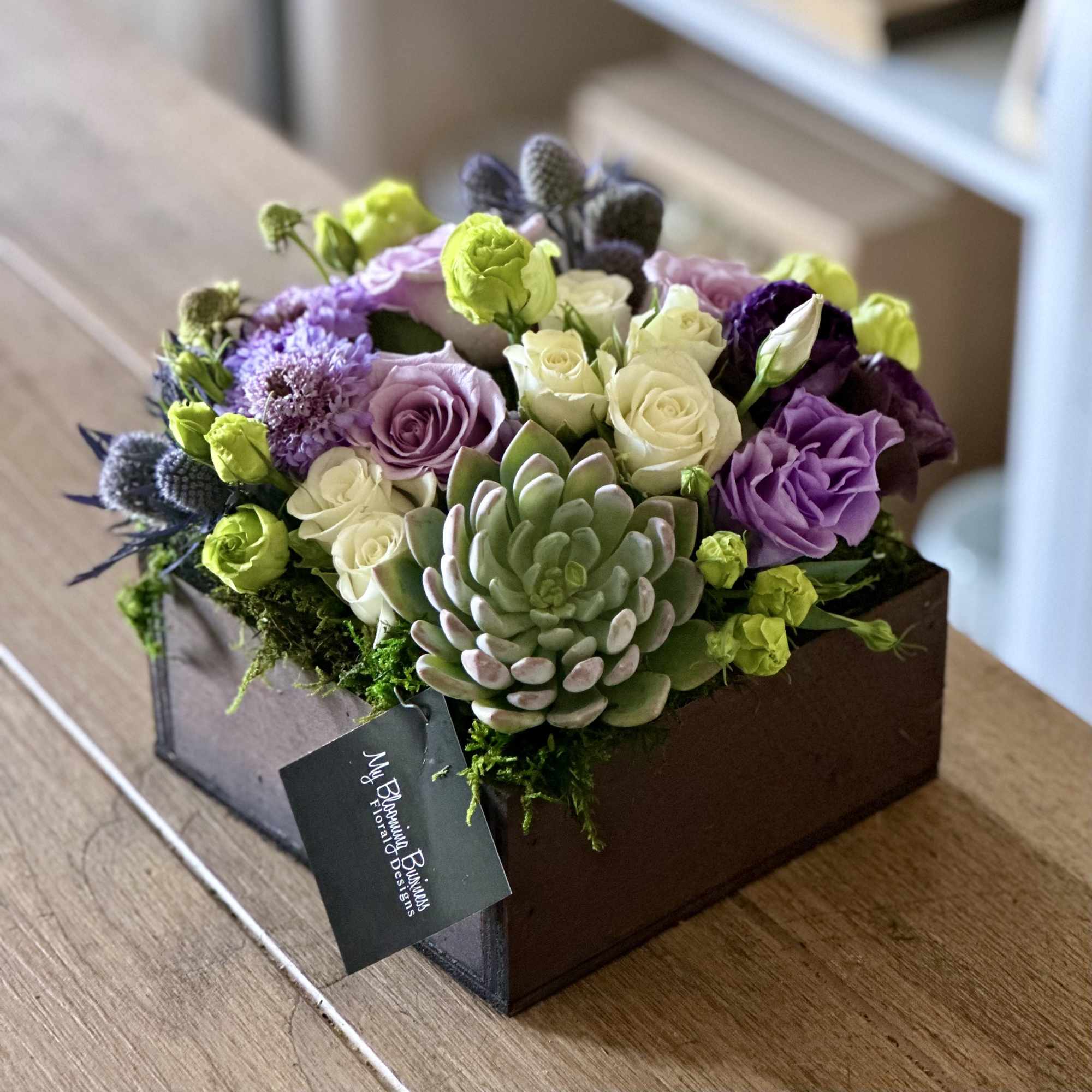Box arrangement of purple and white roses with a succulent centerpiece