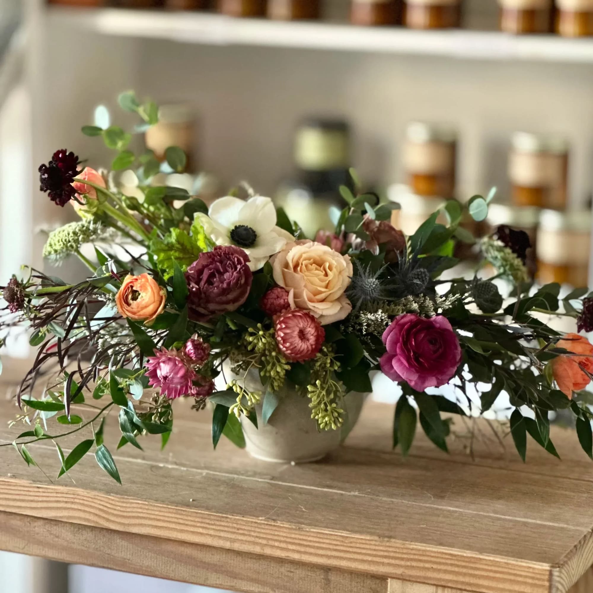 Low floral arrangement with roses, ranunculus, and anemone in a small vase