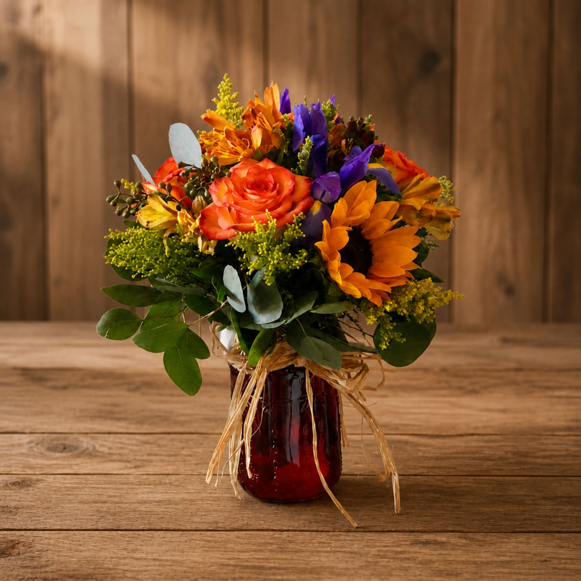Mixed bouquet of orange, purple, and yellow flowers in a red glass vase