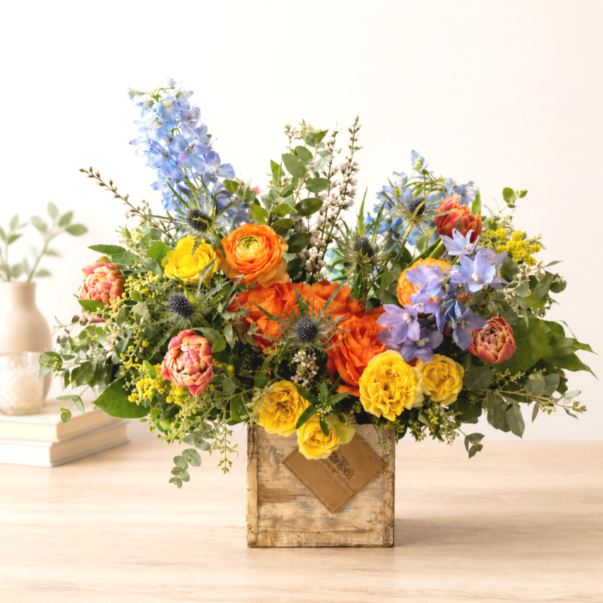 Mixed bouquet in a rustic wooden box with blue, orange, and yellow flowers