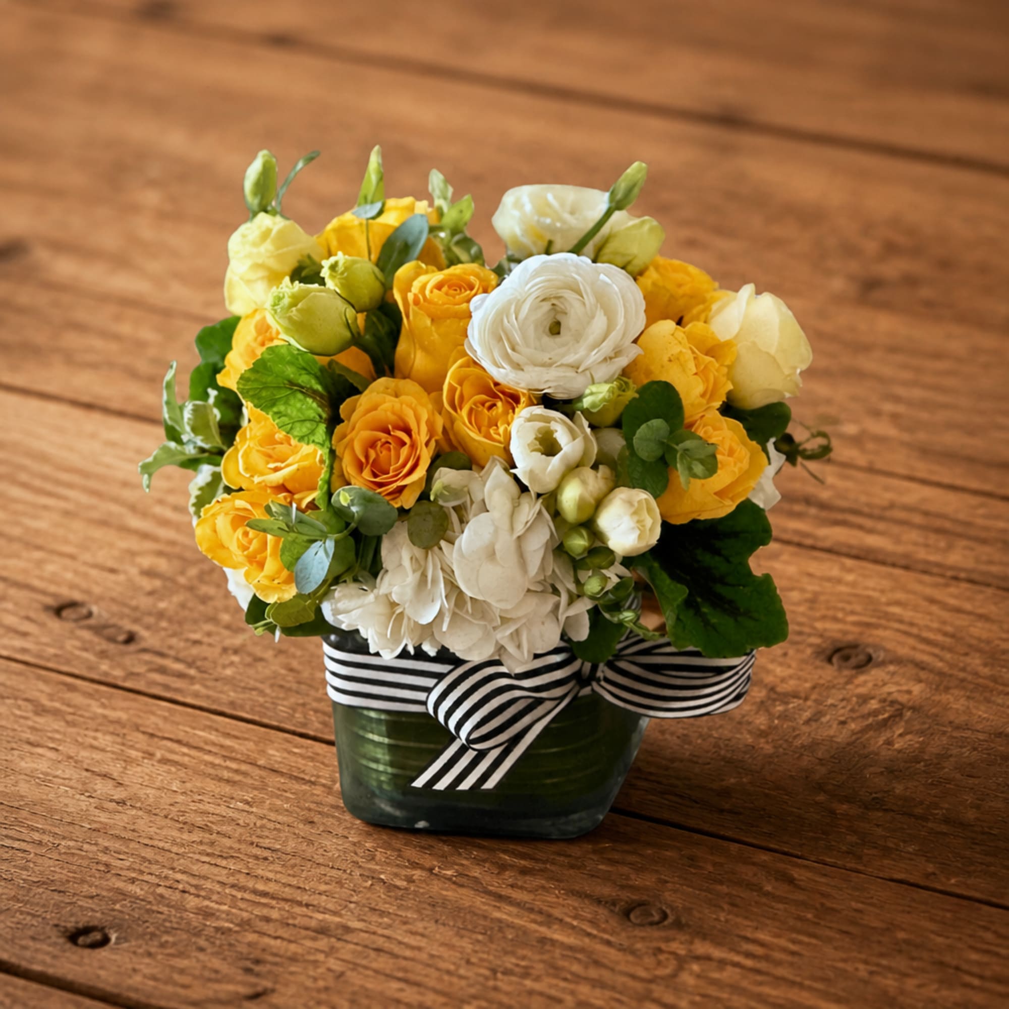 Yellow and white rose arrangement in a square glass vase with a striped ribbon