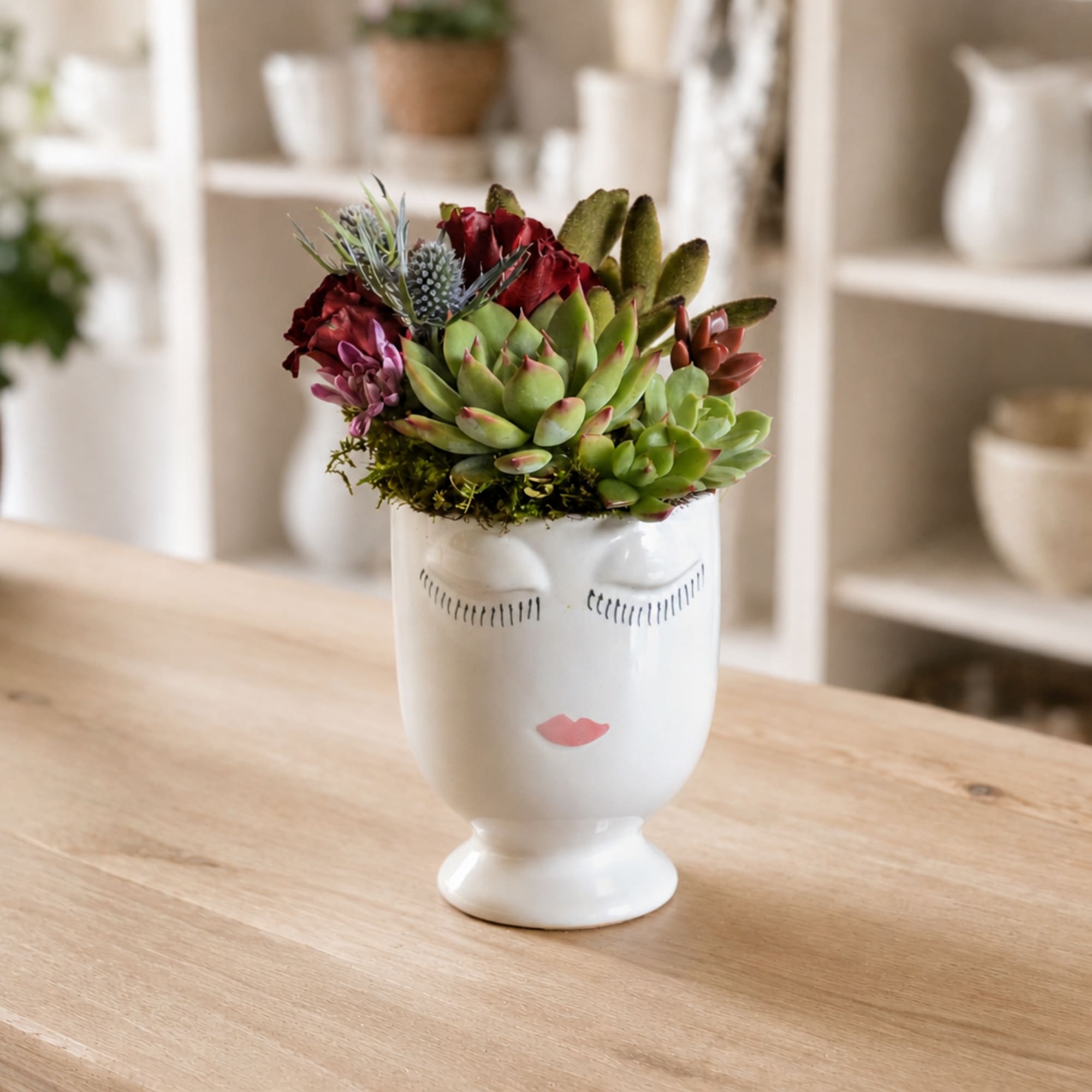 Succulent arrangement in a white face-shaped vase on a wooden table