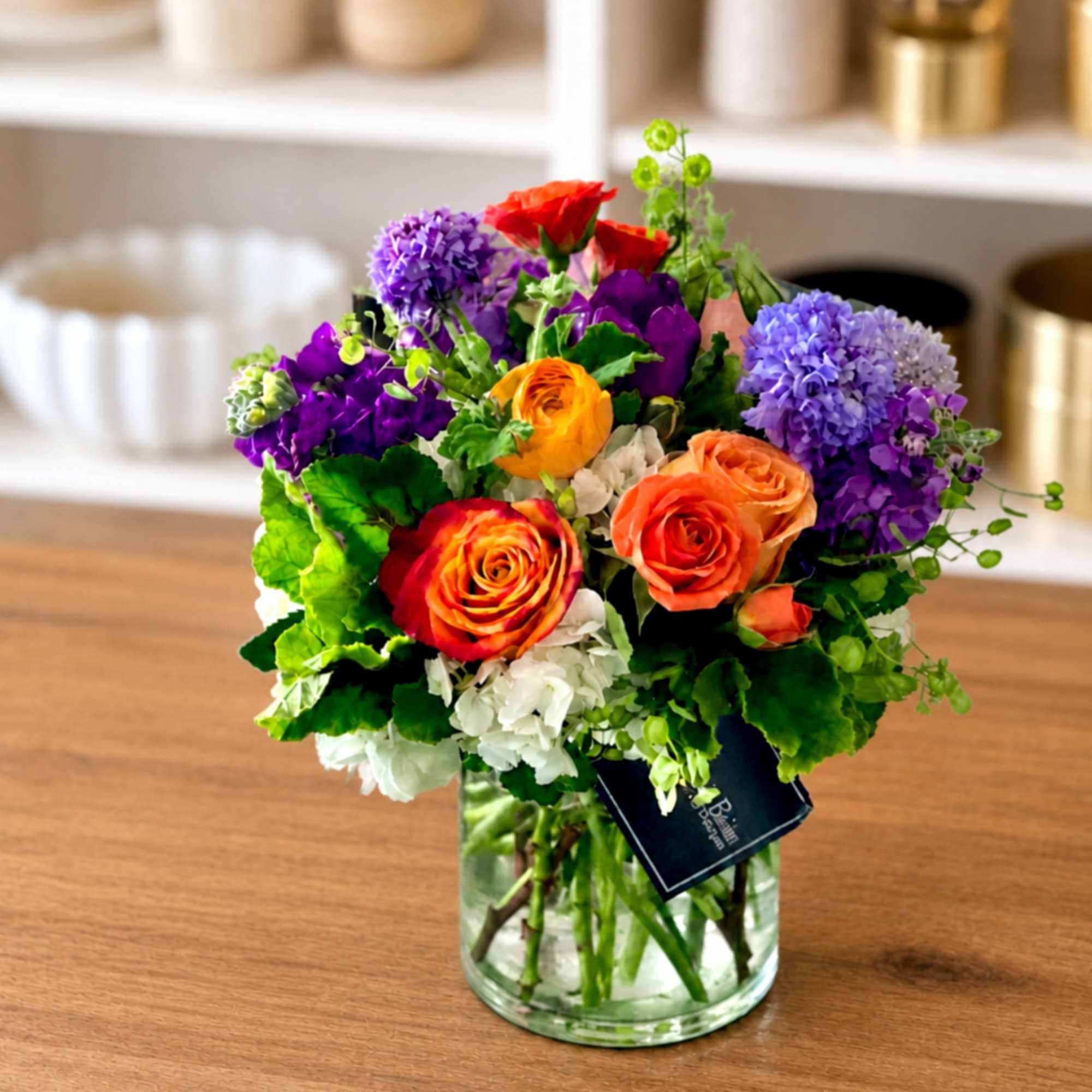 Mixed bouquet of roses, hydrangeas, and purple blooms in a glass vase