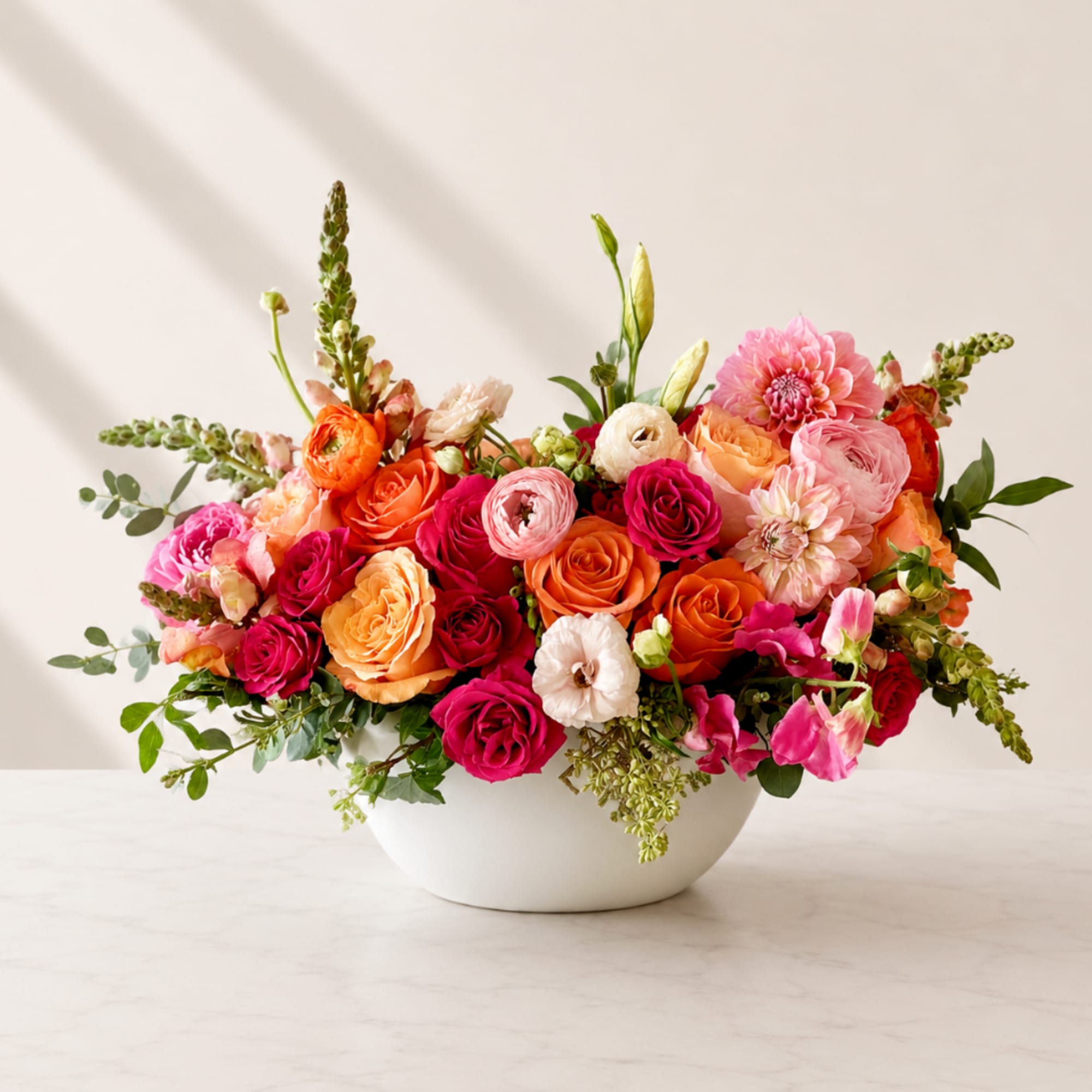 Mixed pink, orange, and white flowers arranged in a white bowl vase