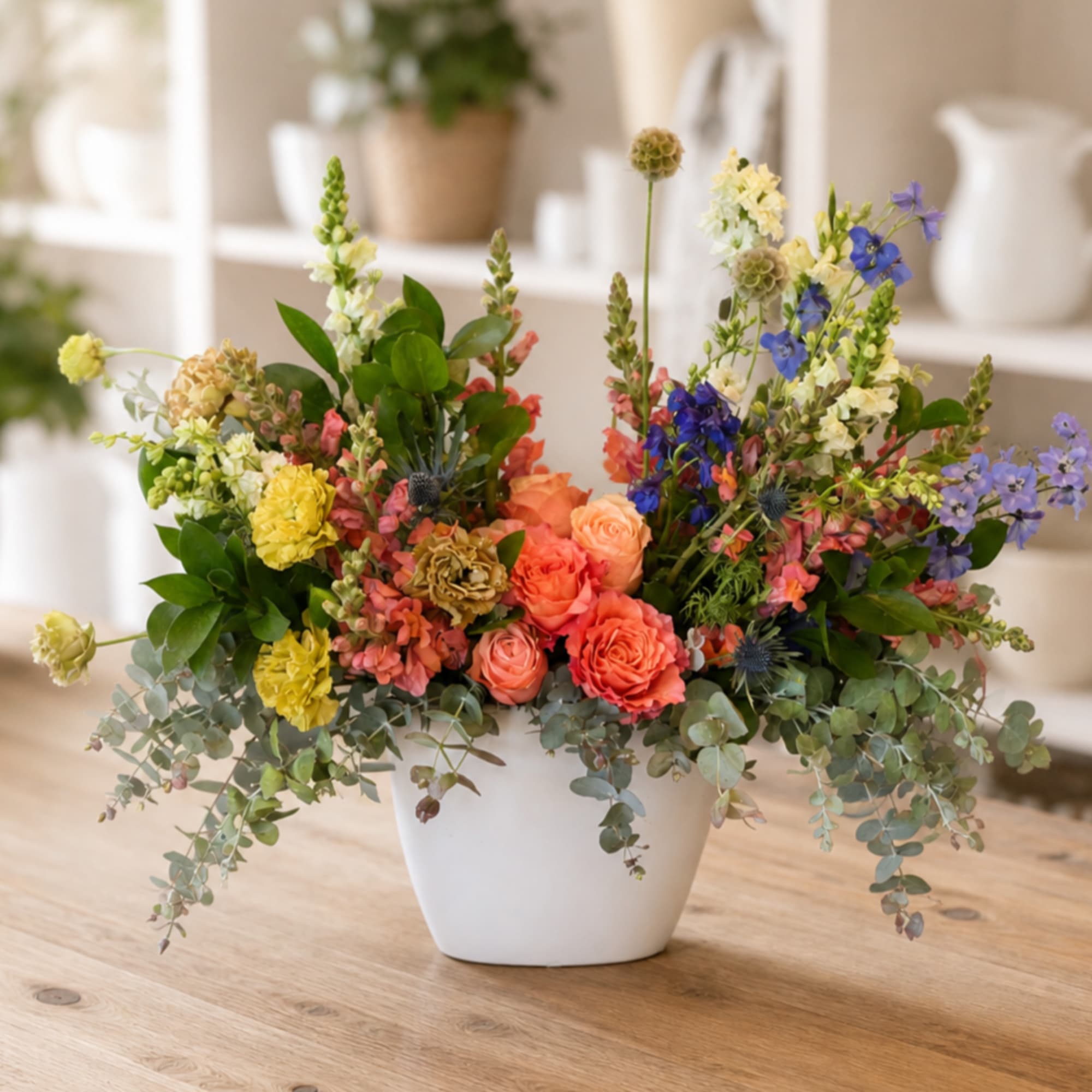 Mixed flower arrangement in a white vase with coral, yellow, blue, and lavender blooms