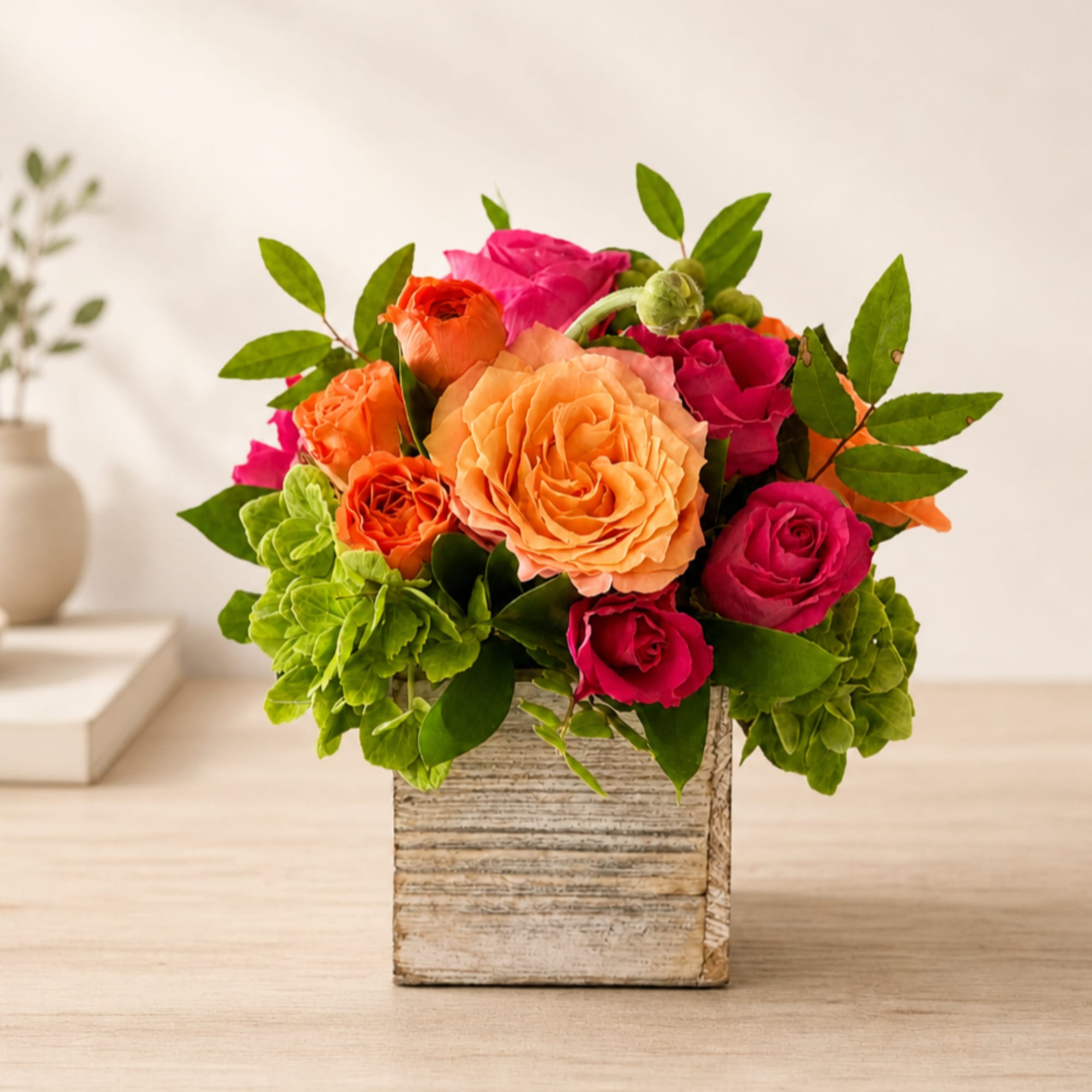 Mixed roses in pink, orange, and peach arranged in a square wooden vase