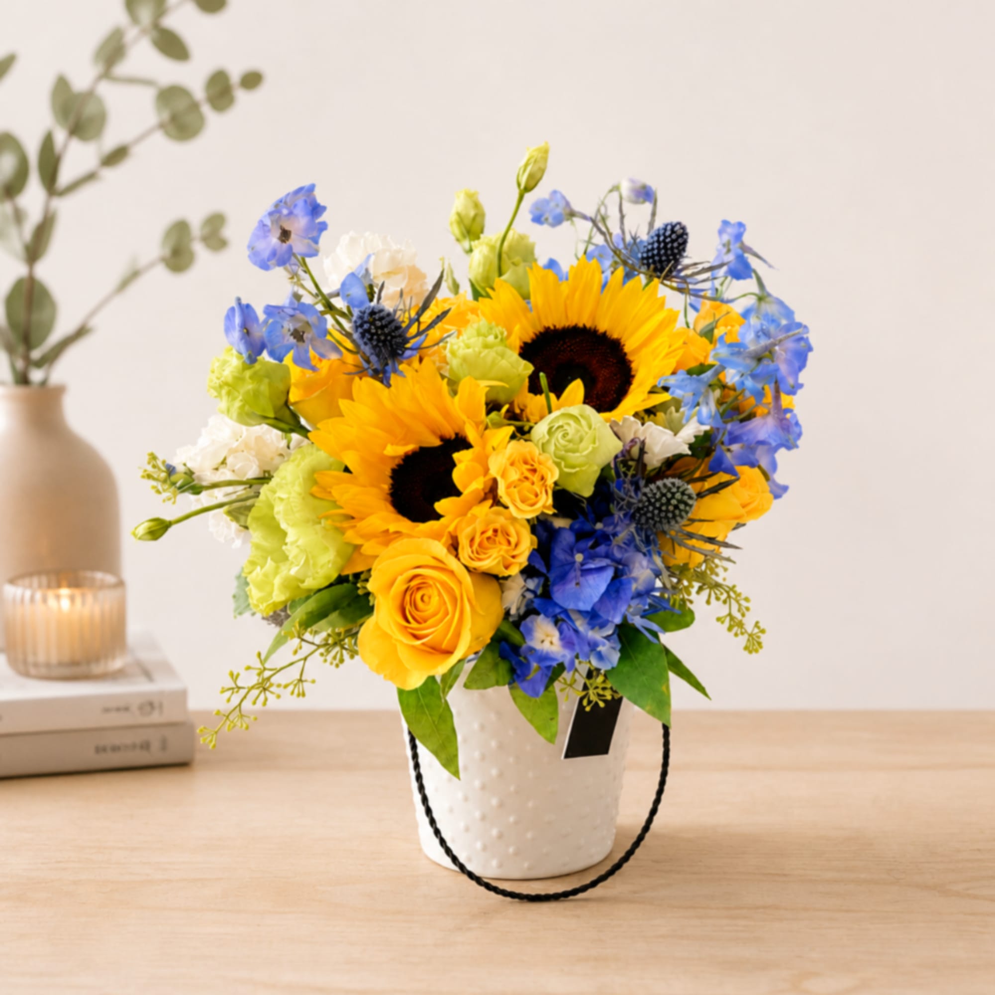 Sunflower bouquet in a white textured bucket with blue and yellow flowers