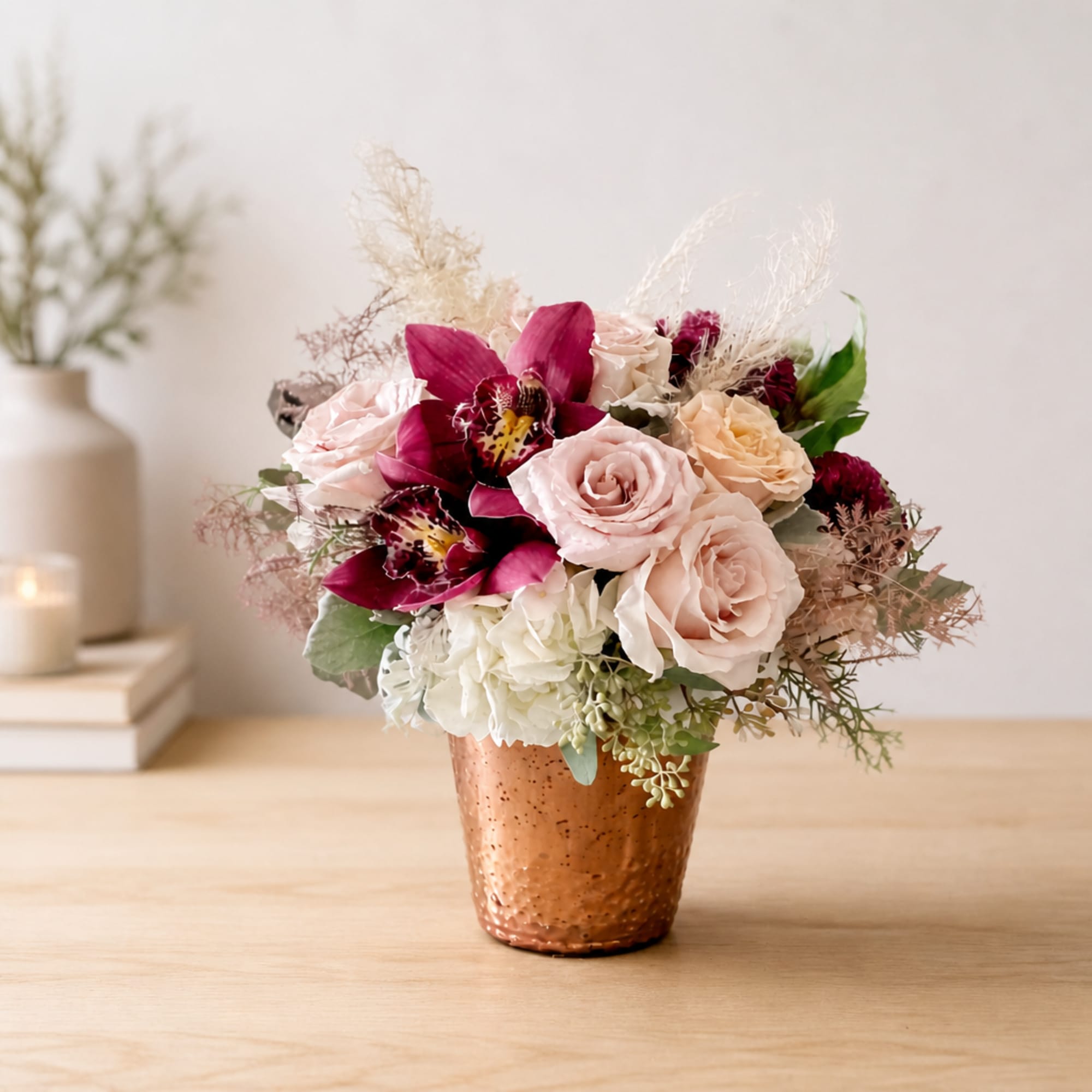 Pink and cream roses with magenta orchids in a copper vase