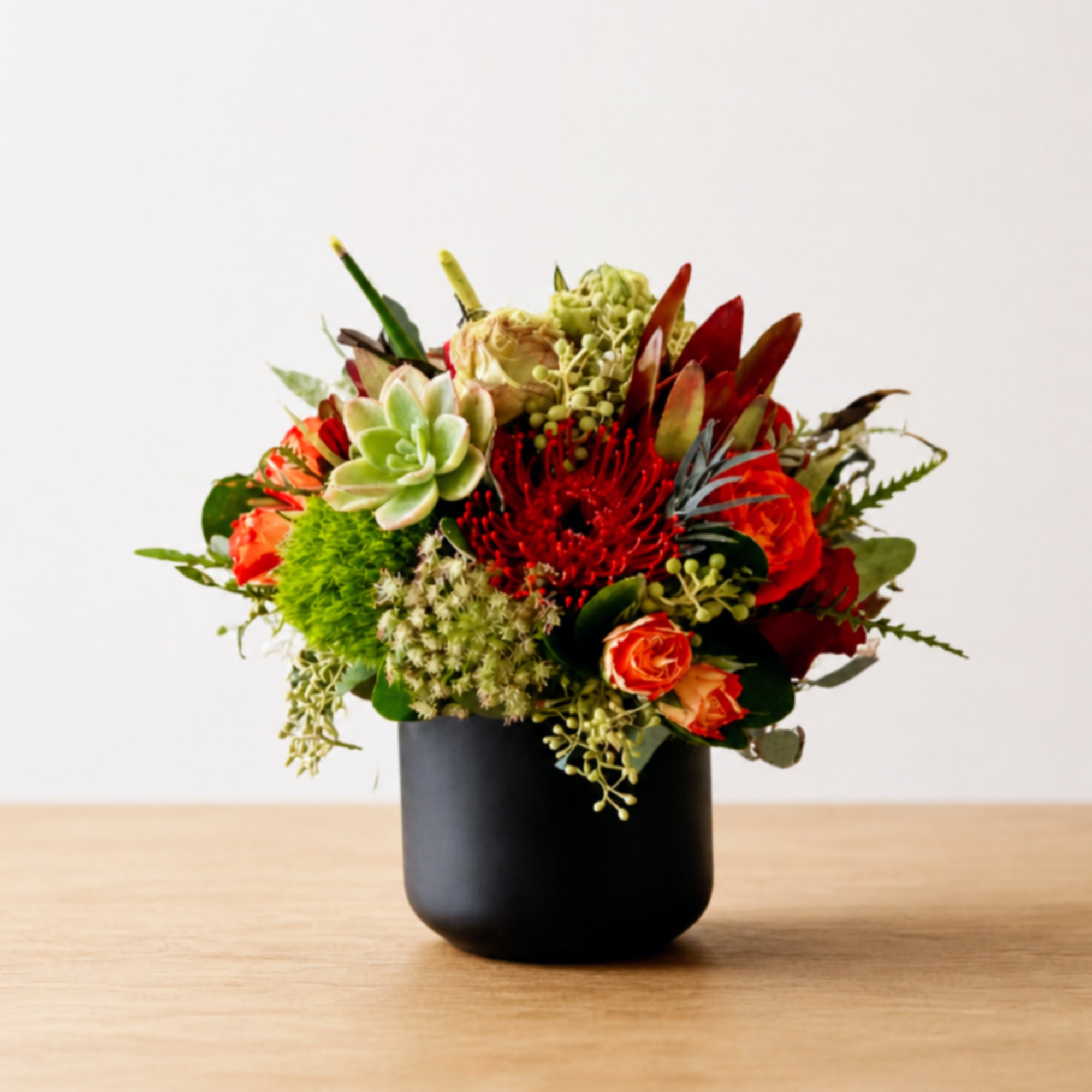 Mixed floral arrangement in a black vase with red, orange, and green blooms