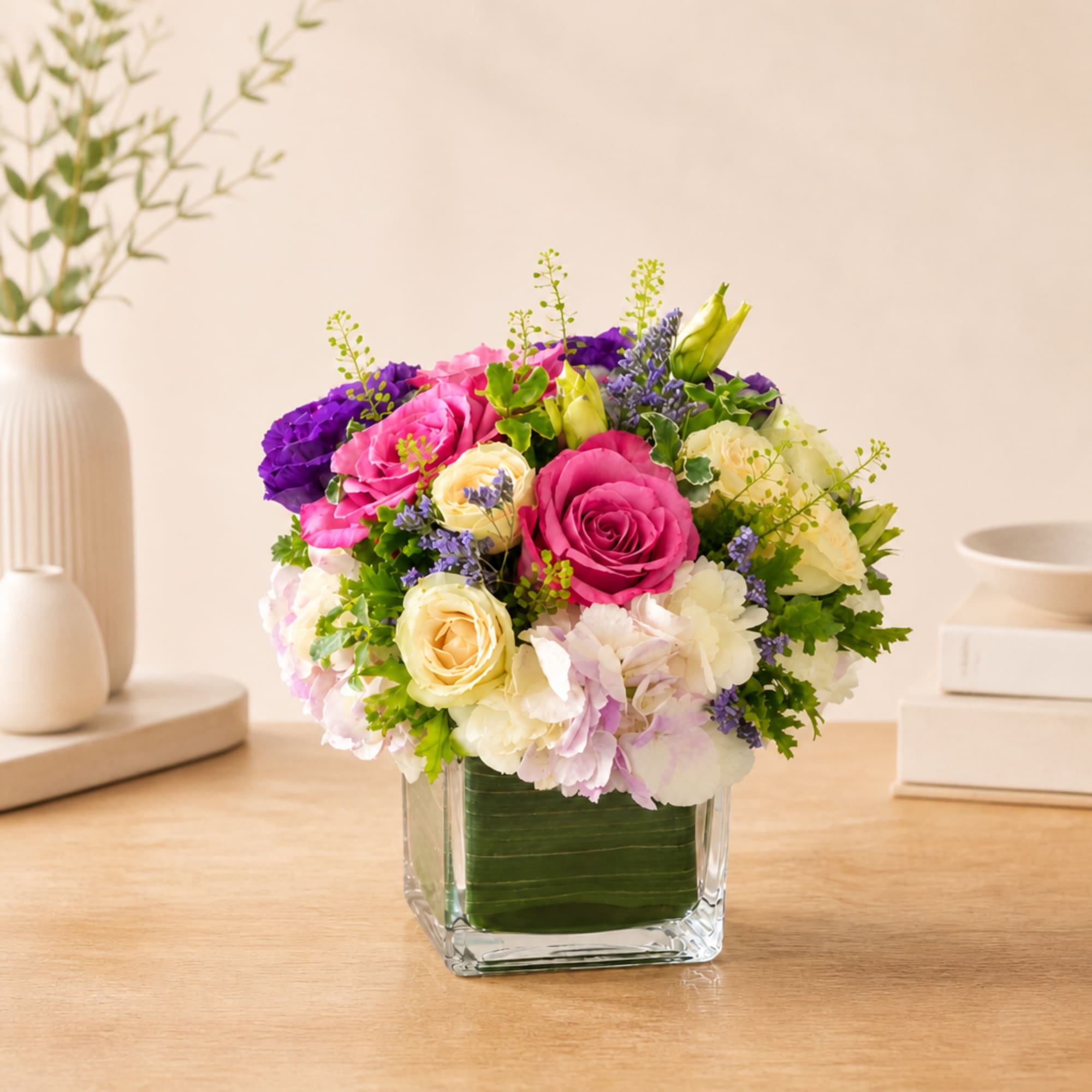 Mixed pink, purple, and white flowers arranged in a clear square vase
