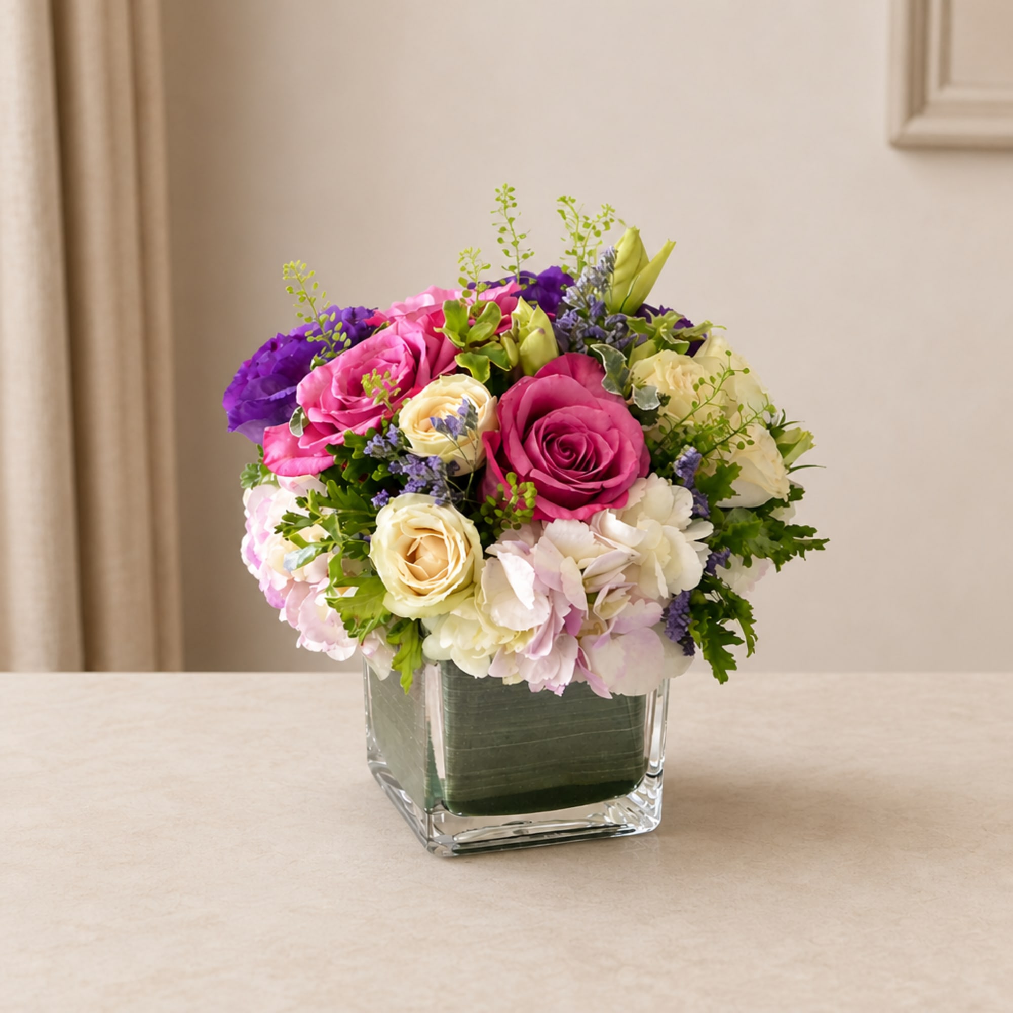 Mixed pink, white, and purple flower arrangement in a clear square vase