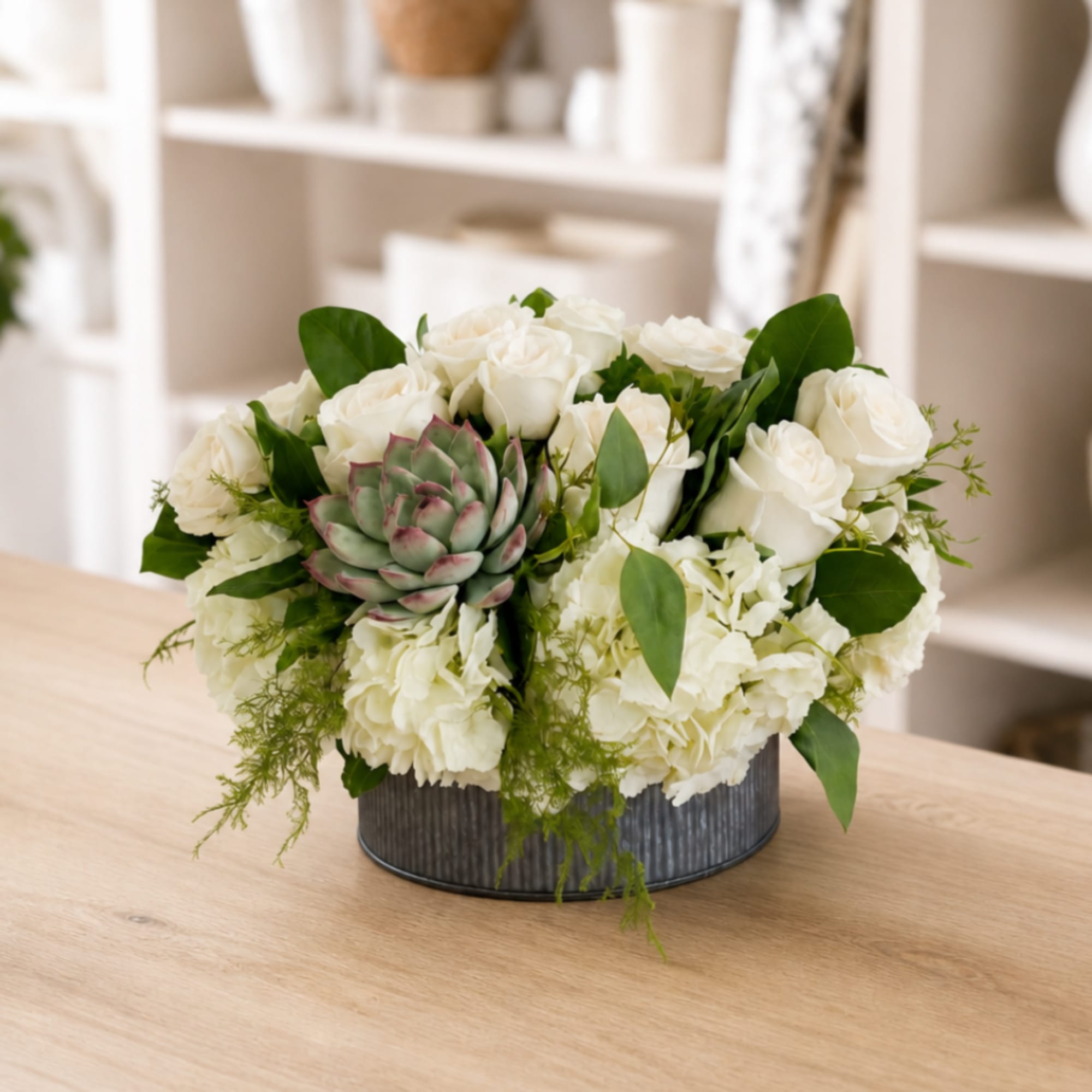 White rose and hydrangea arrangement in a gray metal container with a succulent accent