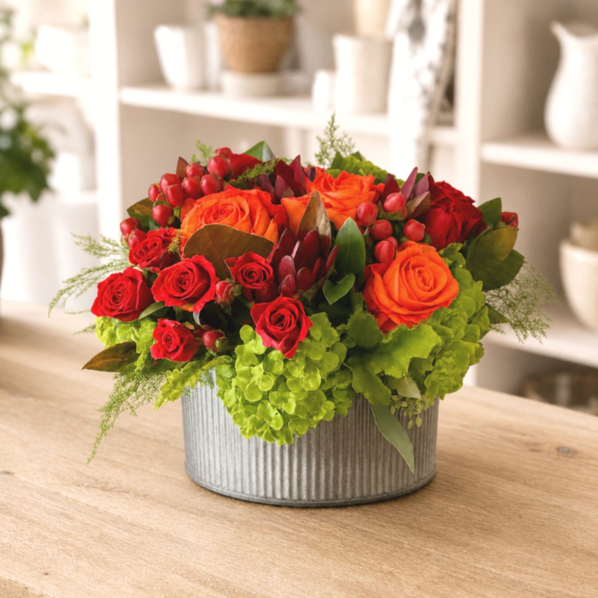 Red and orange roses arranged in a ribbed metal container