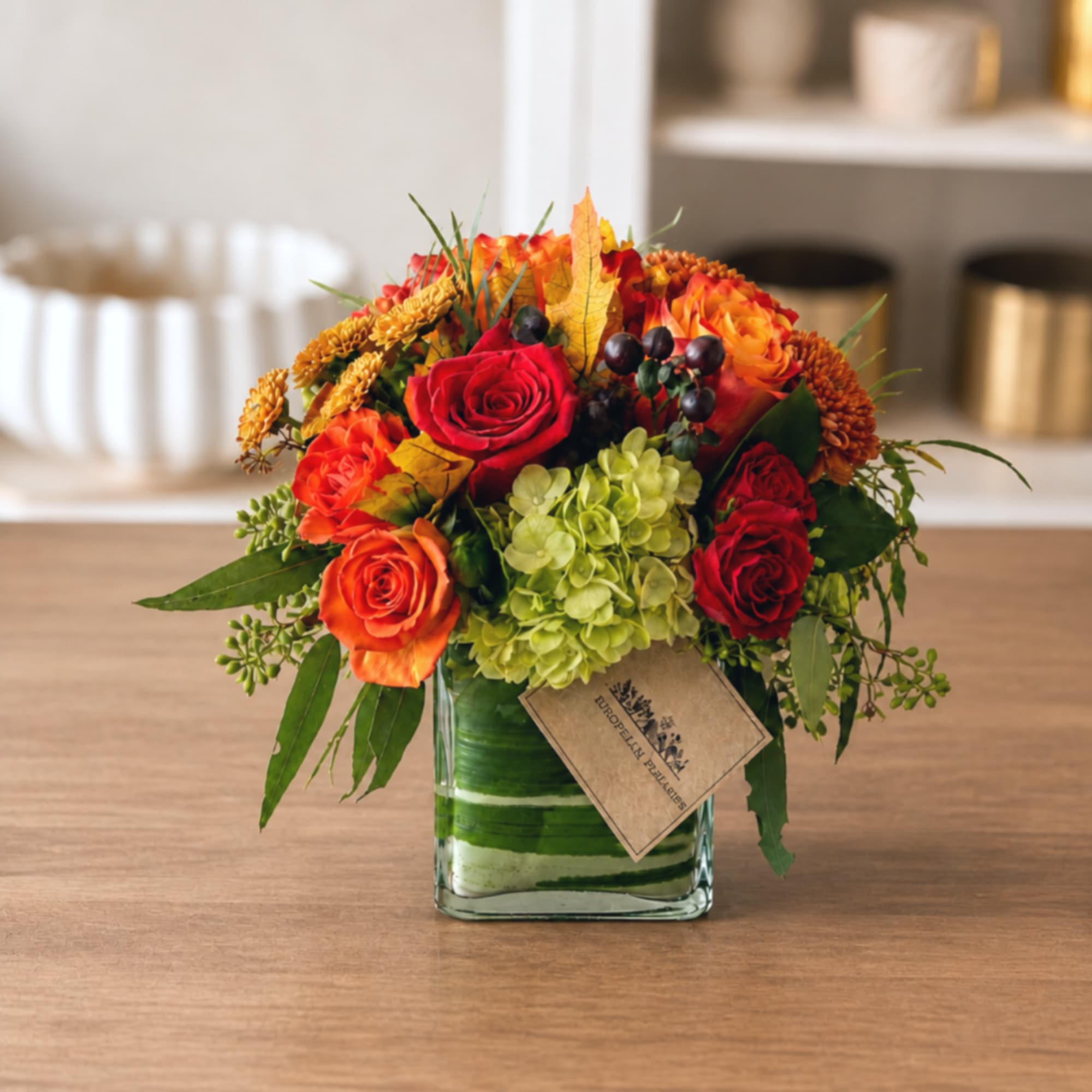 Autumn bouquet of red and orange roses in a square glass vase