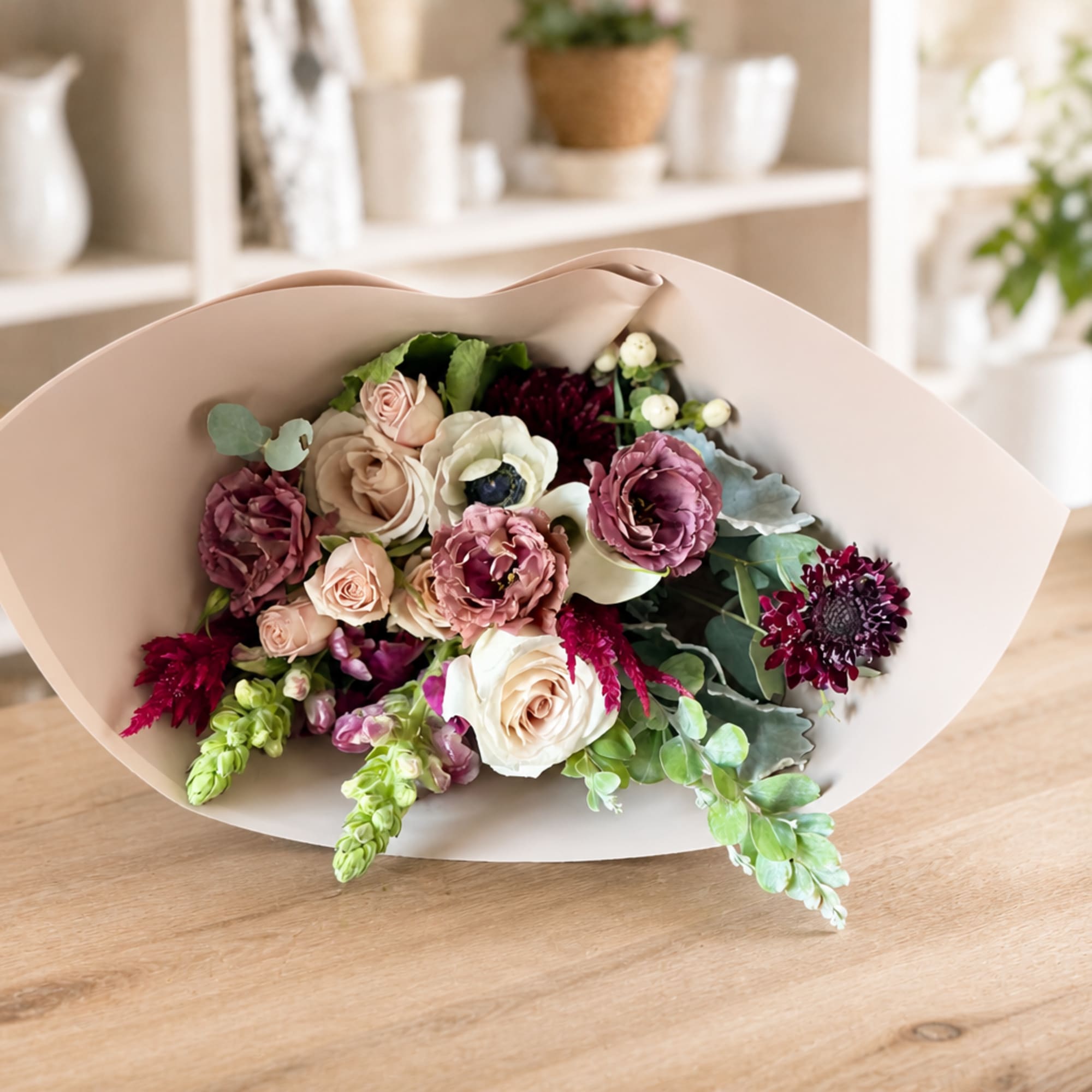 Bouquet of blush, cream, and burgundy flowers wrapped in pale paper