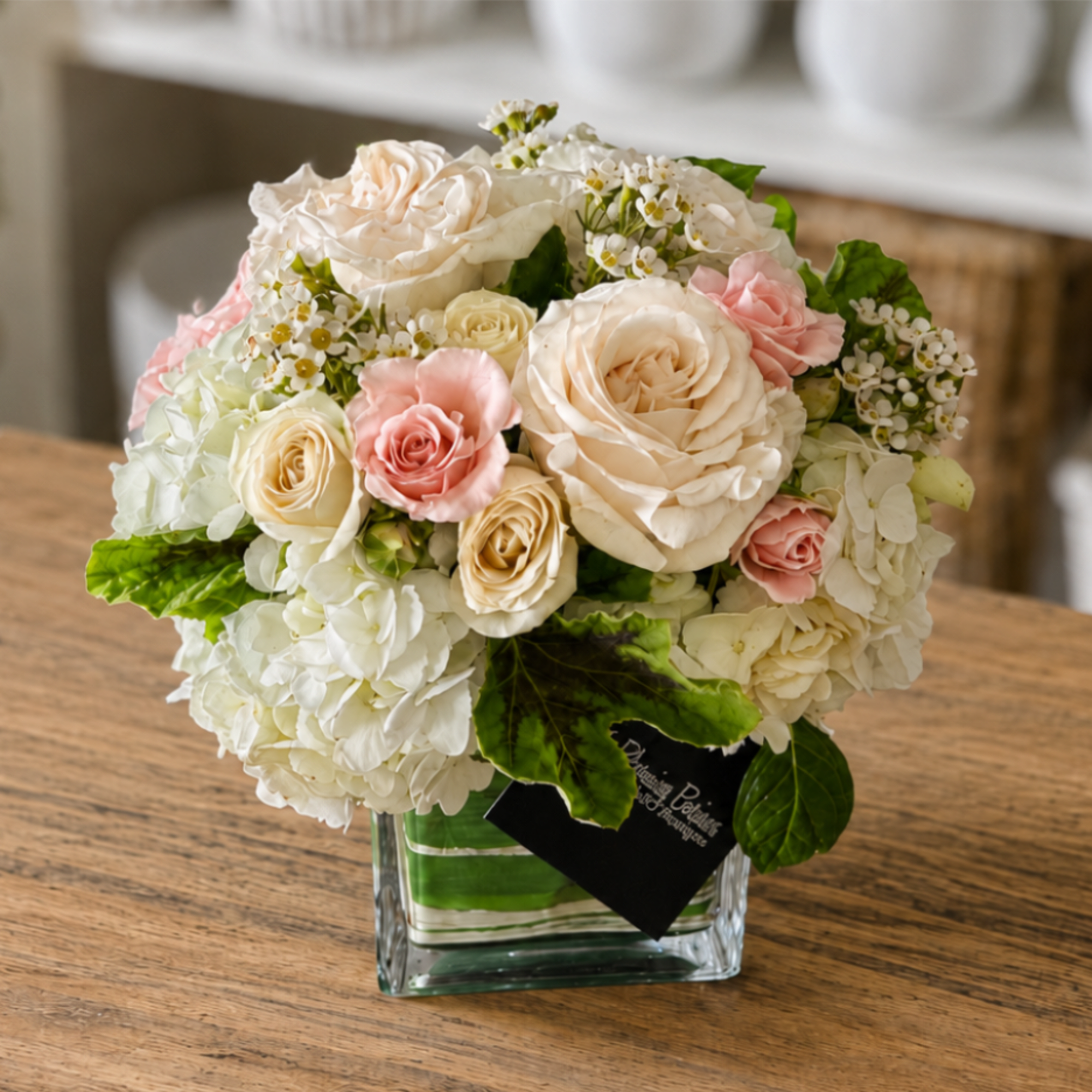 Compact bouquet of cream and pink roses in a clear square vase