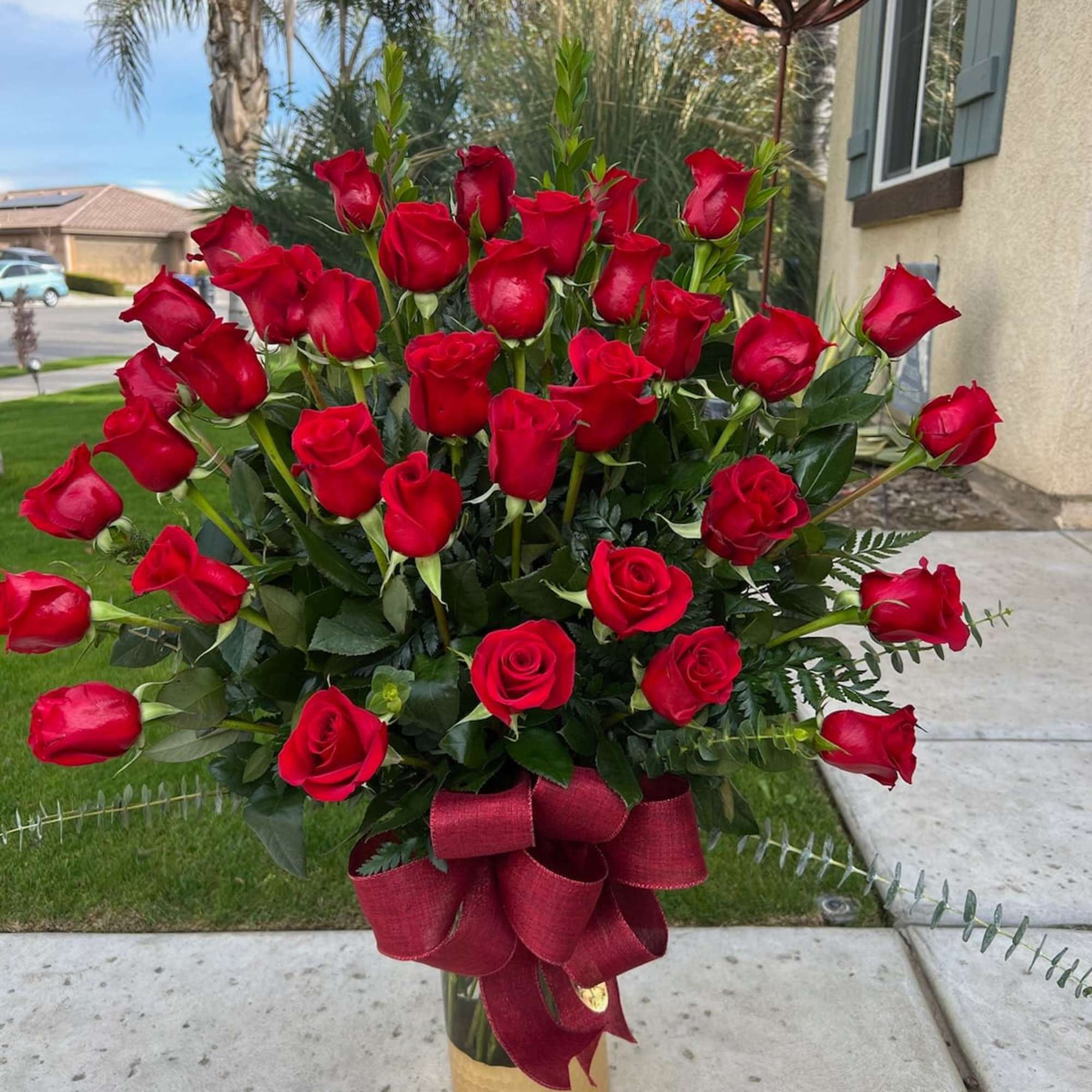 Tall bouquet of red roses in a gold vase with a burgundy ribbon