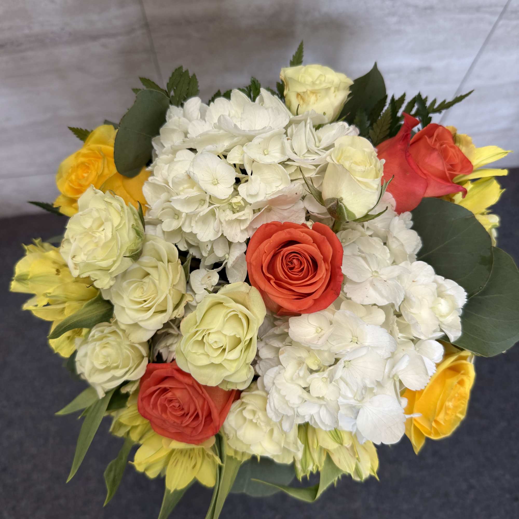 A soft, elegant arrangement featuring orange and yellow roses, white hydrangea, and