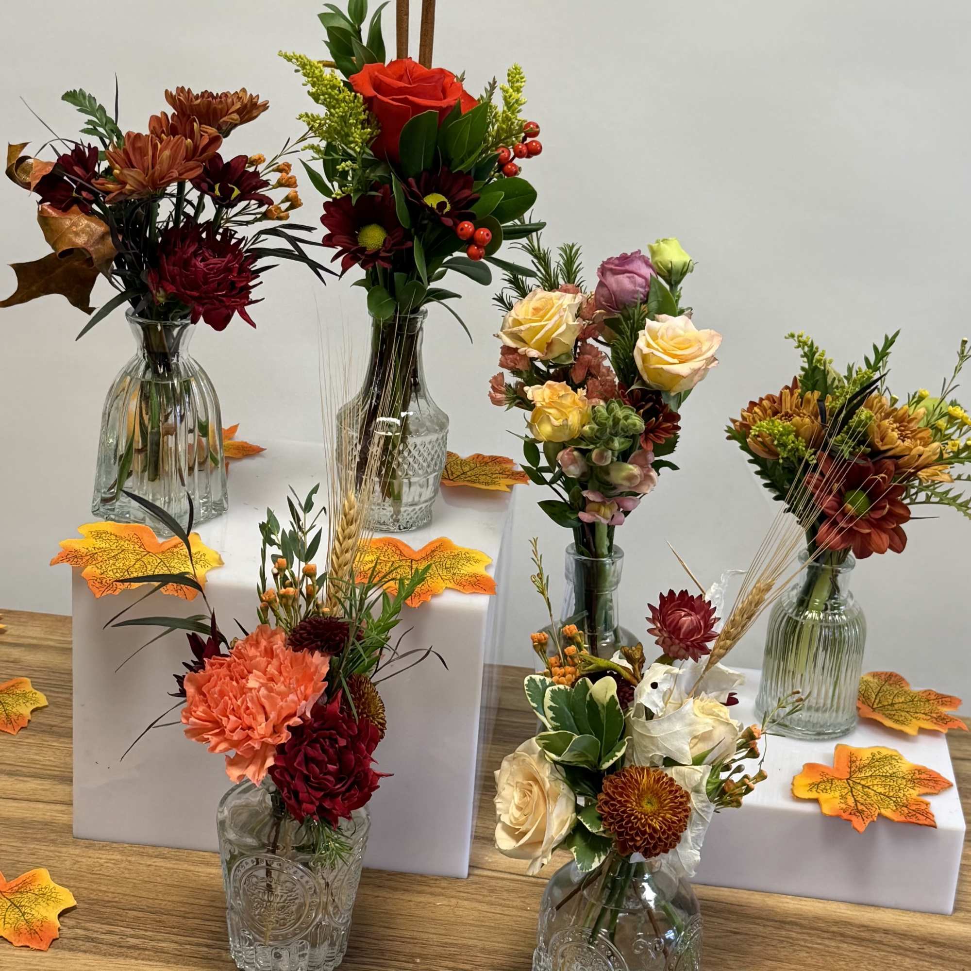 Assorted fall floral arrangements in glass vases on white risers