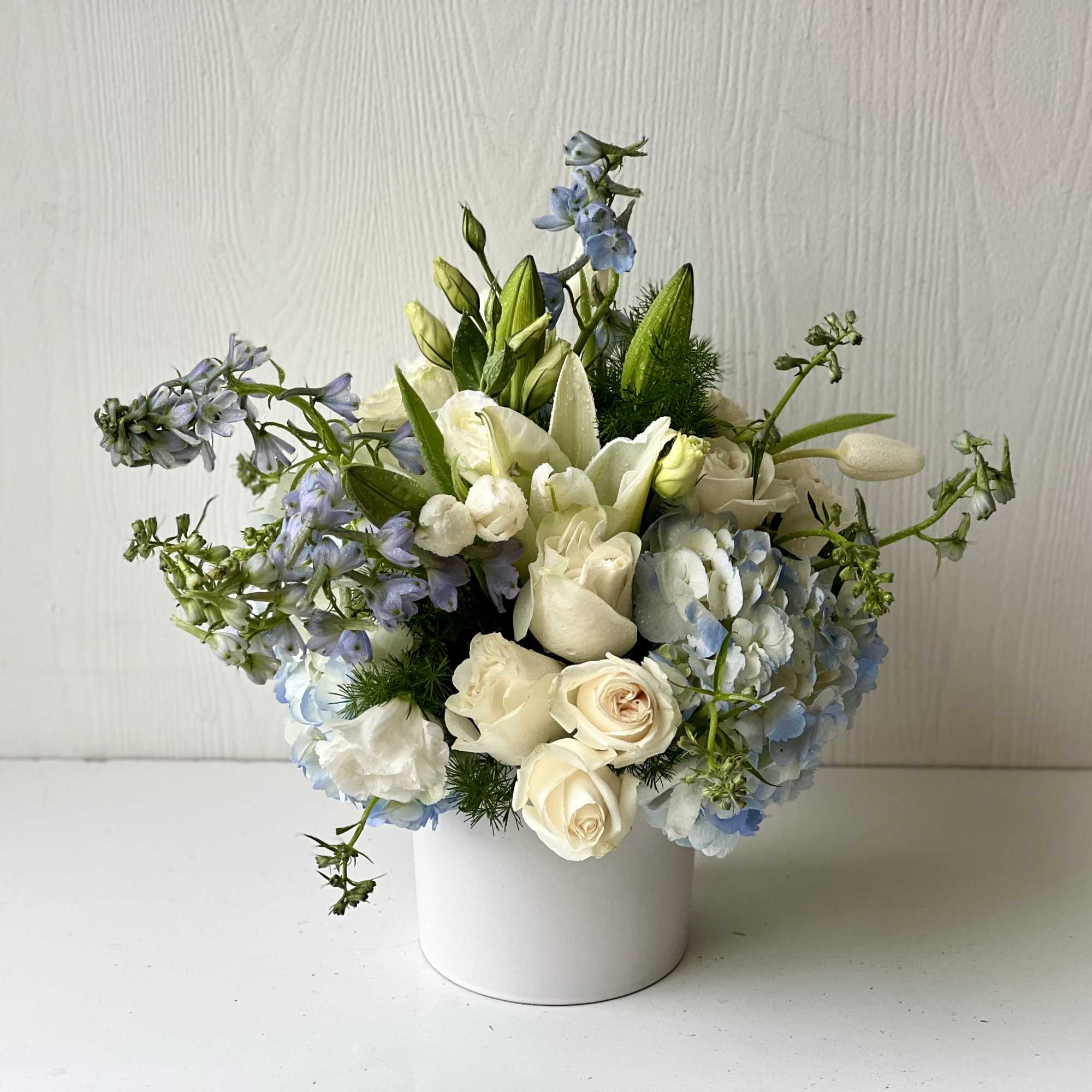 White and pale blue floral arrangement in a white vase
