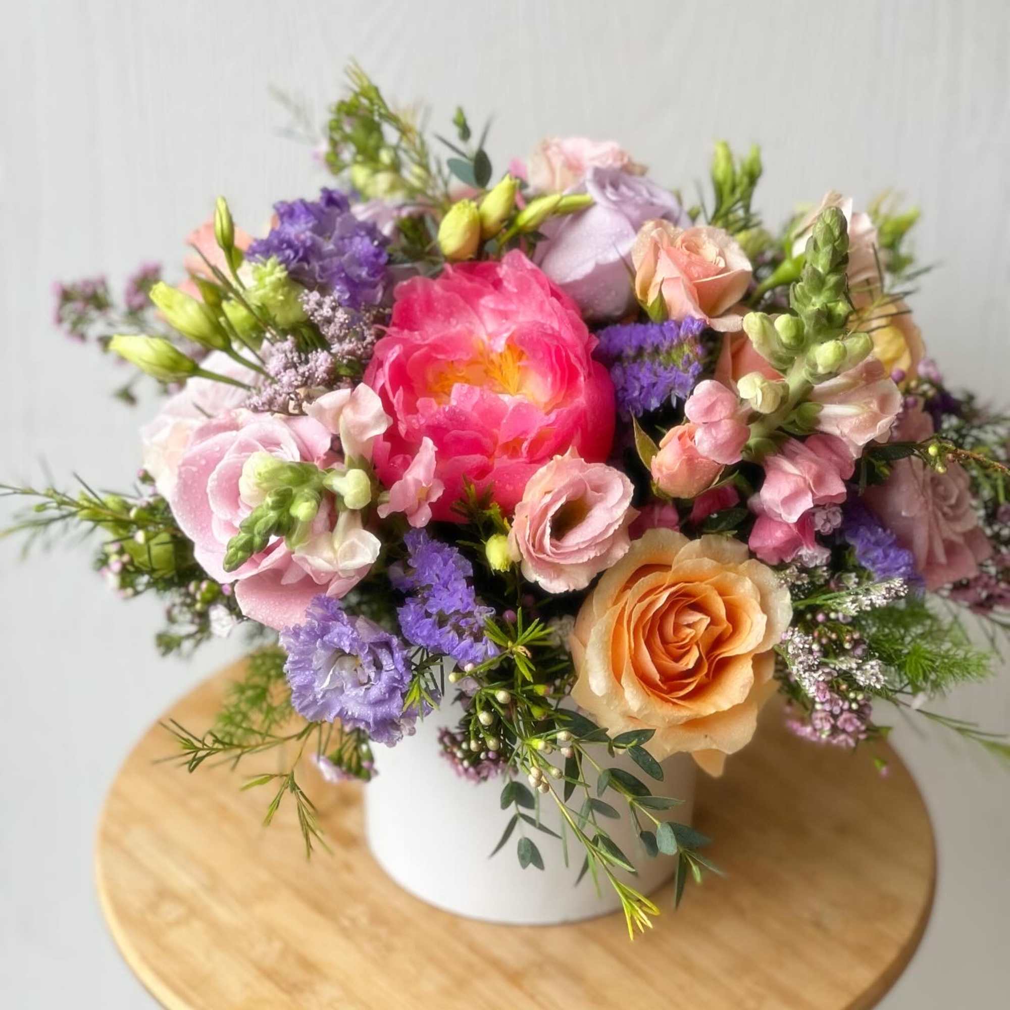 Mixed bouquet of pink, peach, and purple flowers in a white vase