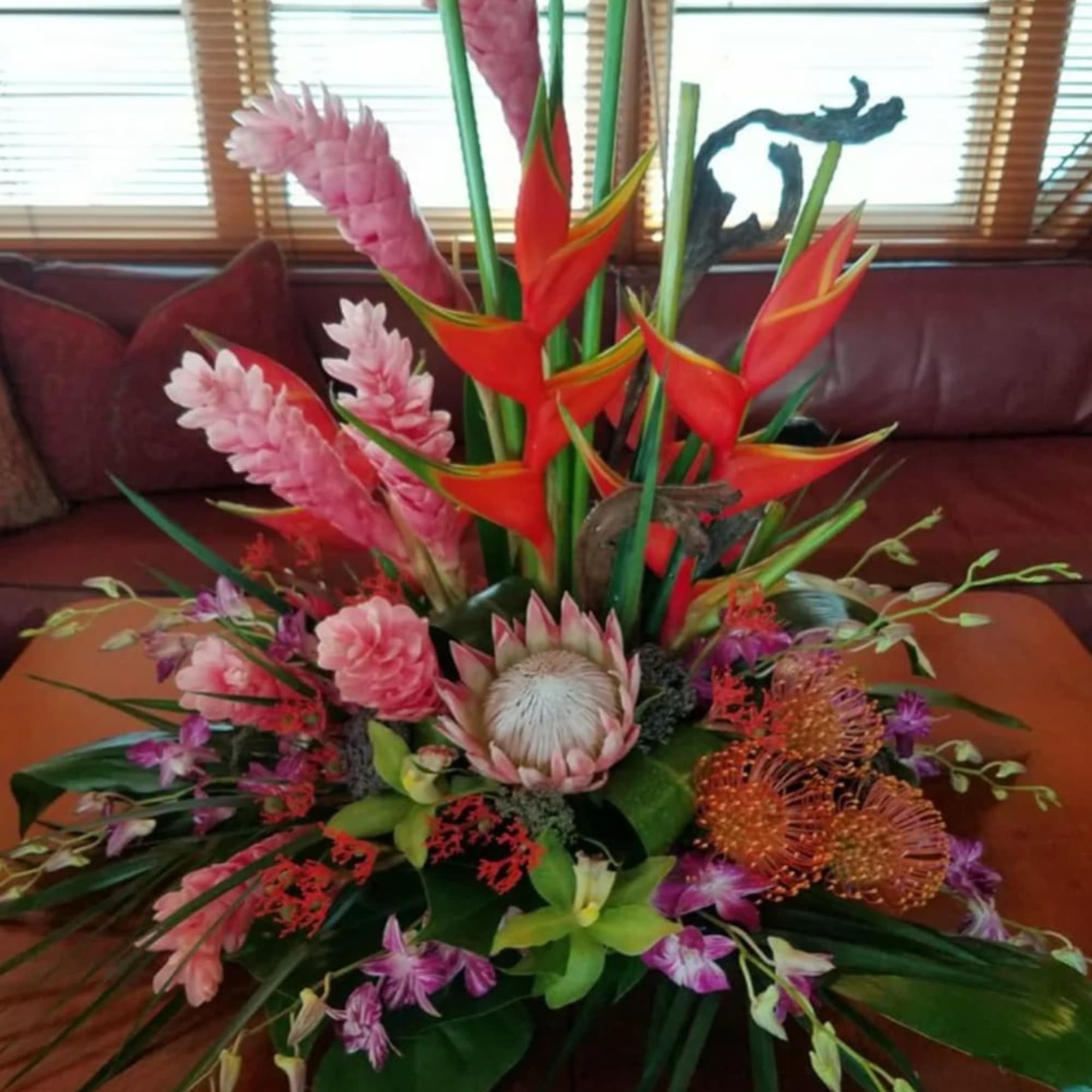 Tropical floral arrangement with pink and red blooms in a low container