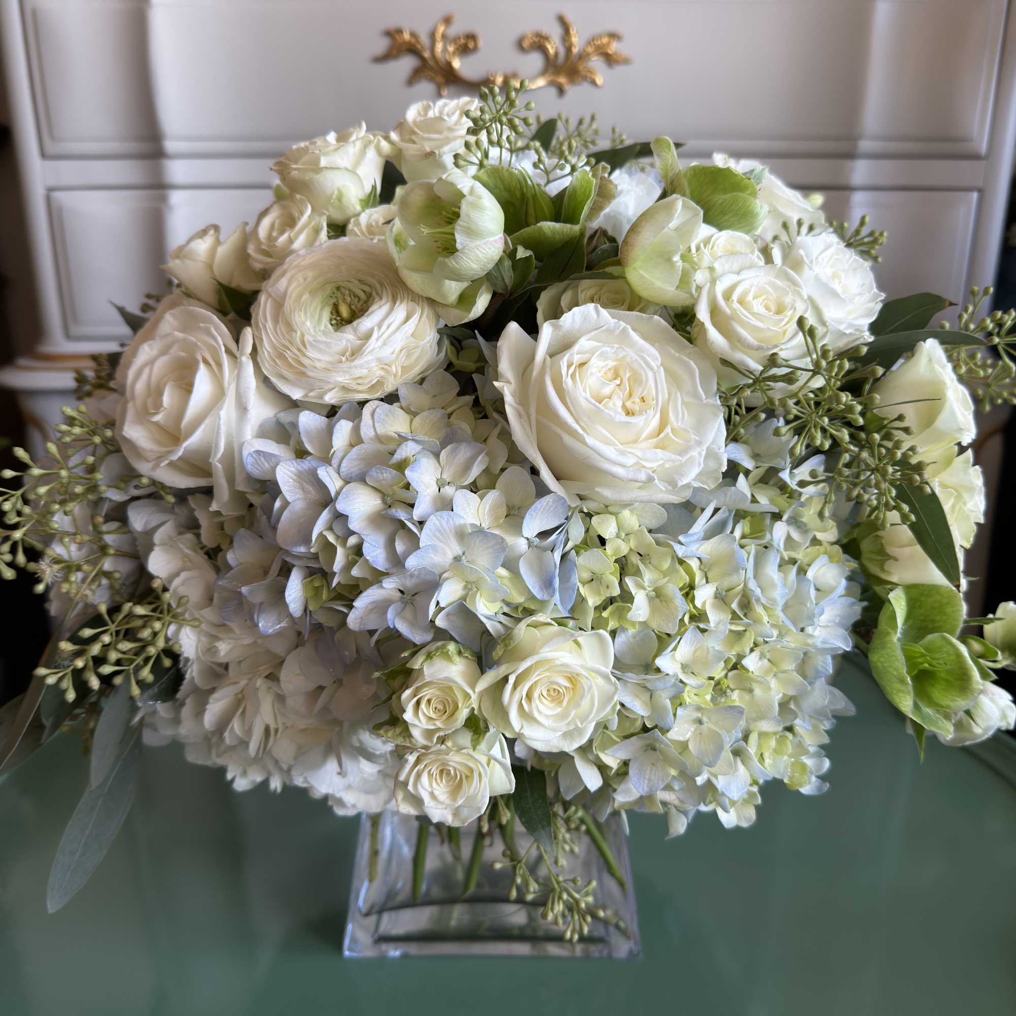 An elegant clear glass vase brimming with periwinkle blue hydrangea, white roses