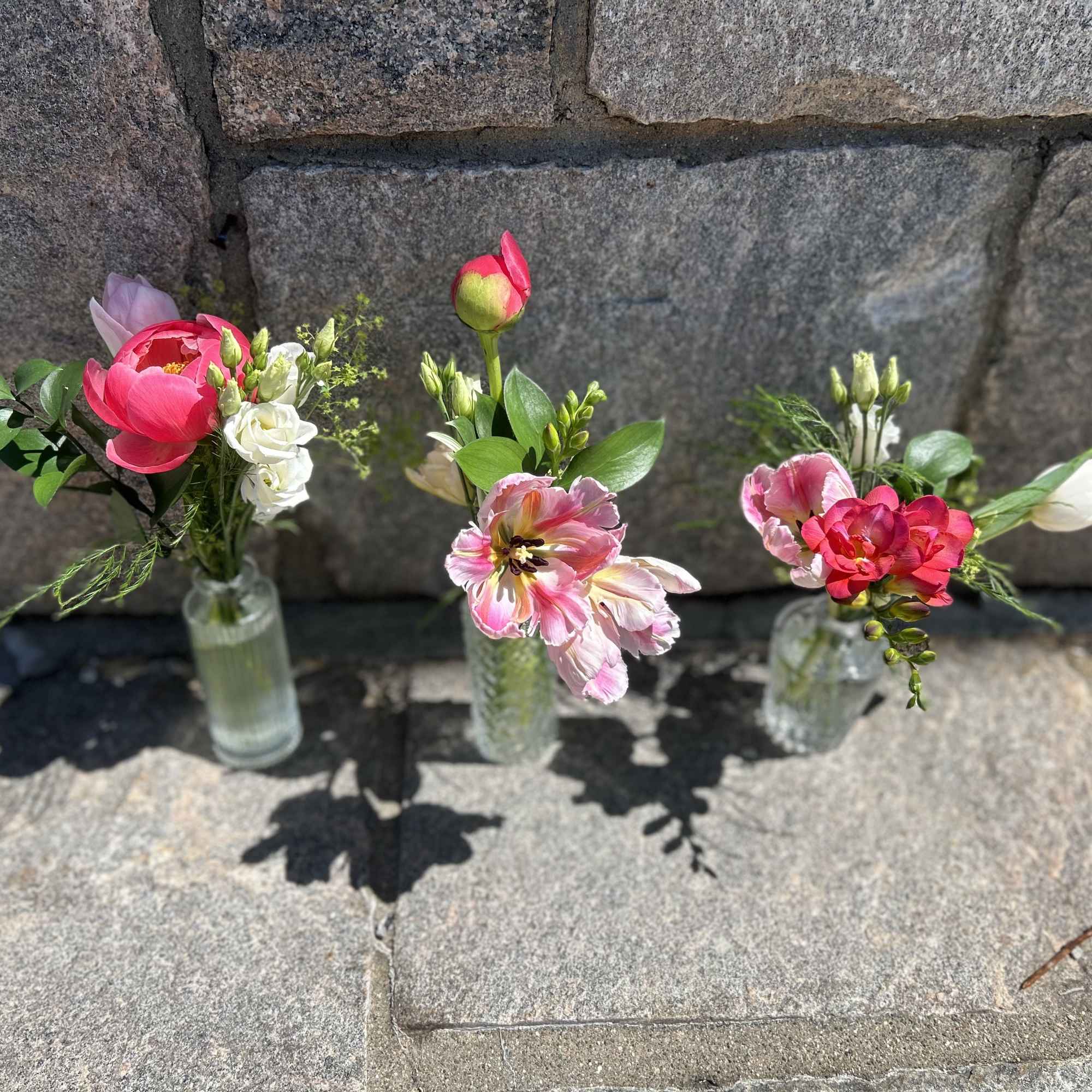 Three small floral arrangements in clear glass bottles on stone steps