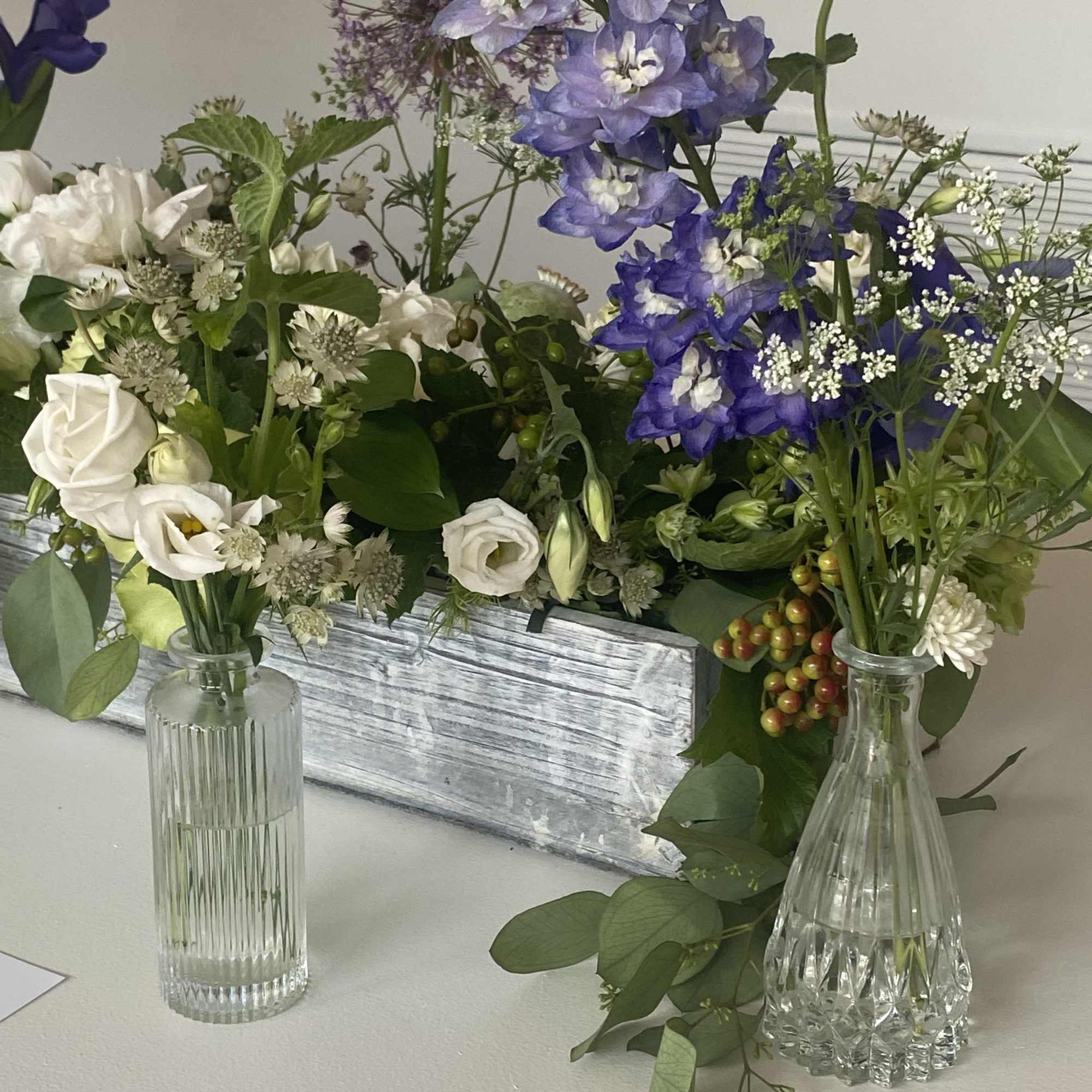 White and purple floral arrangement in glass vases with greenery