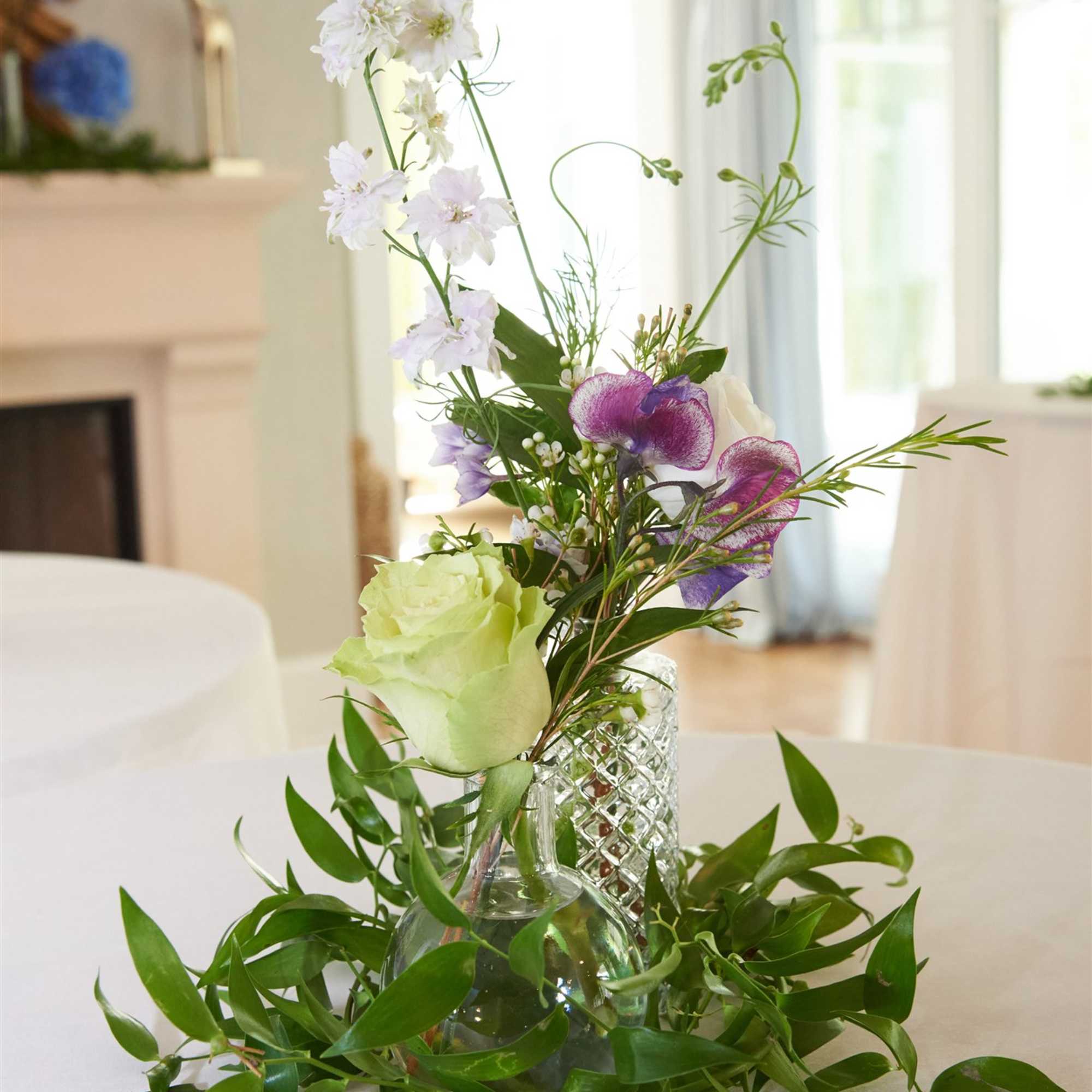 Tall floral arrangement in a glass vase with white, green, and purple blooms