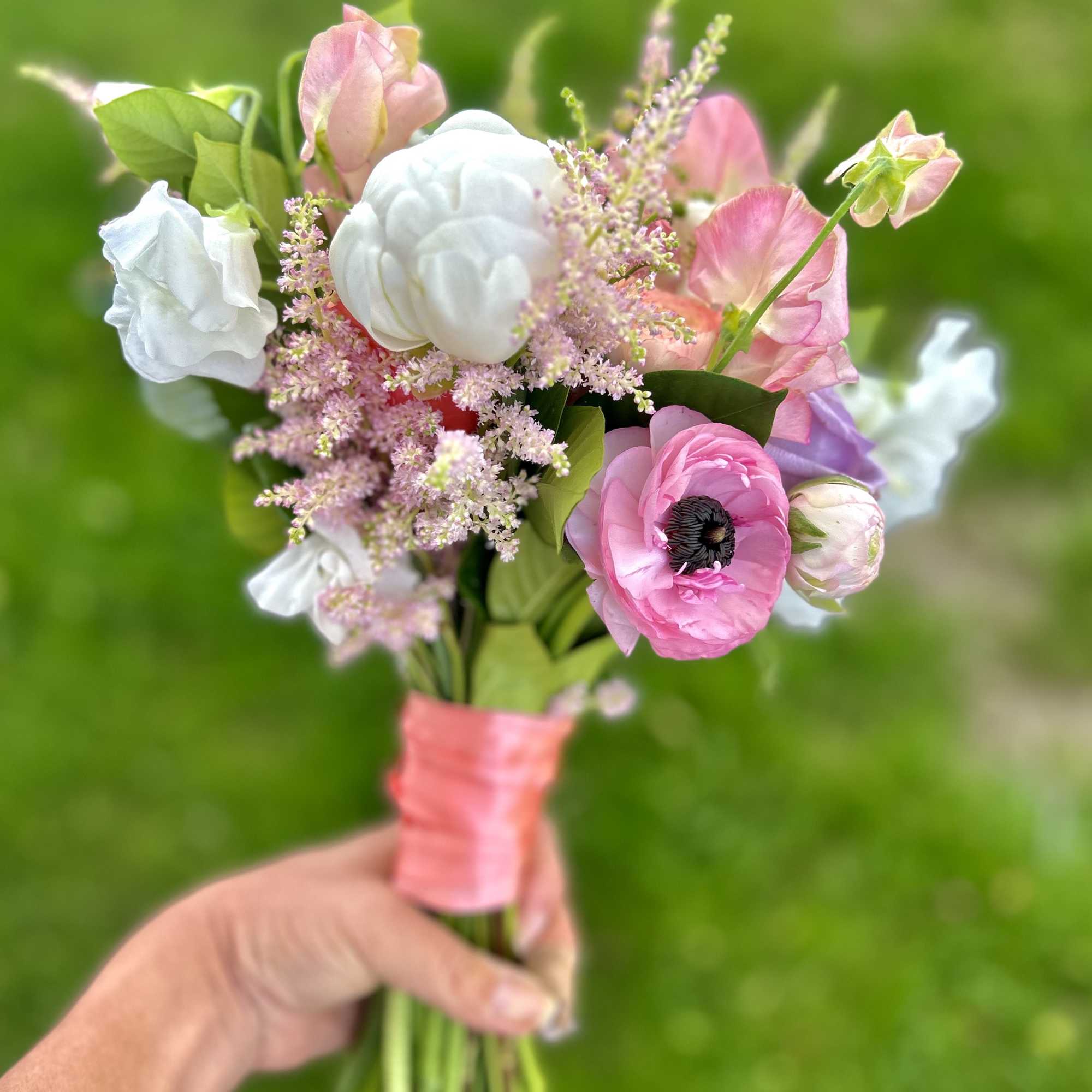 Handheld bouquet of pink and white flowers tied with pink ribbon