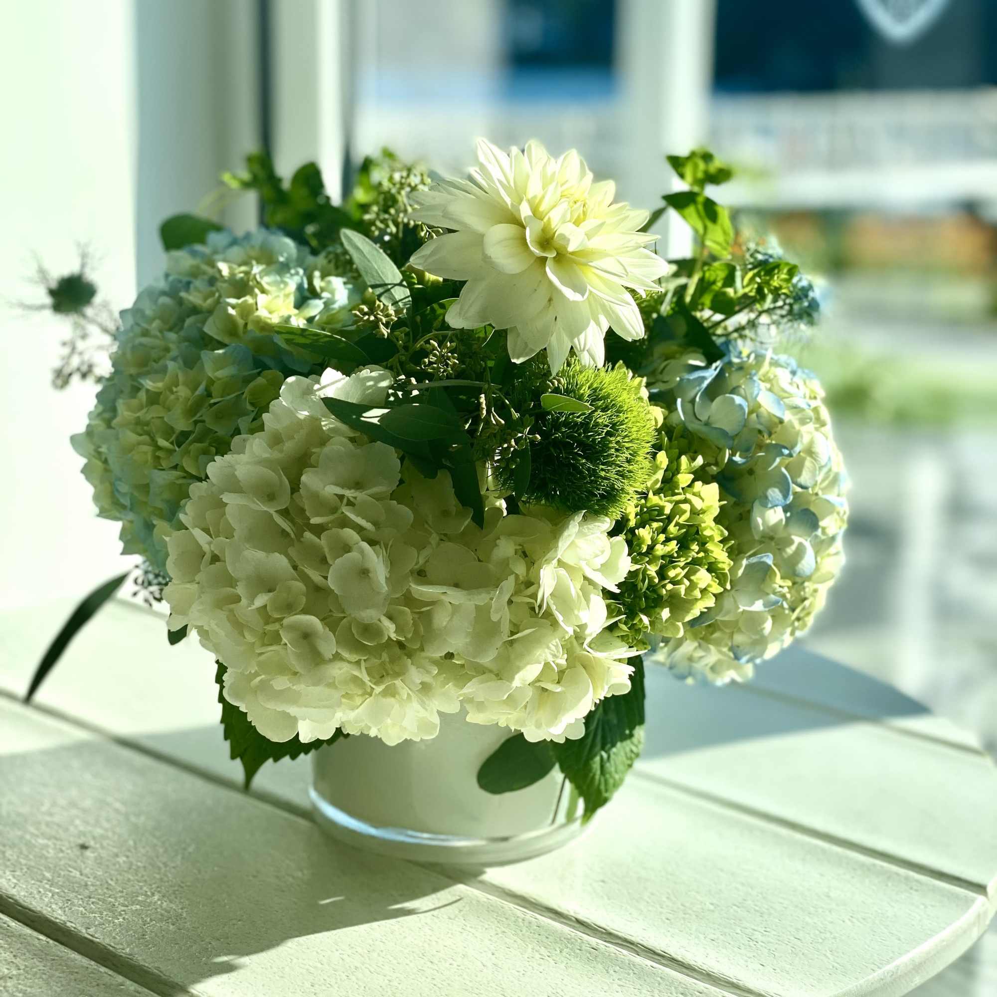 White and pale blue hydrangea arrangement in a clear glass vase